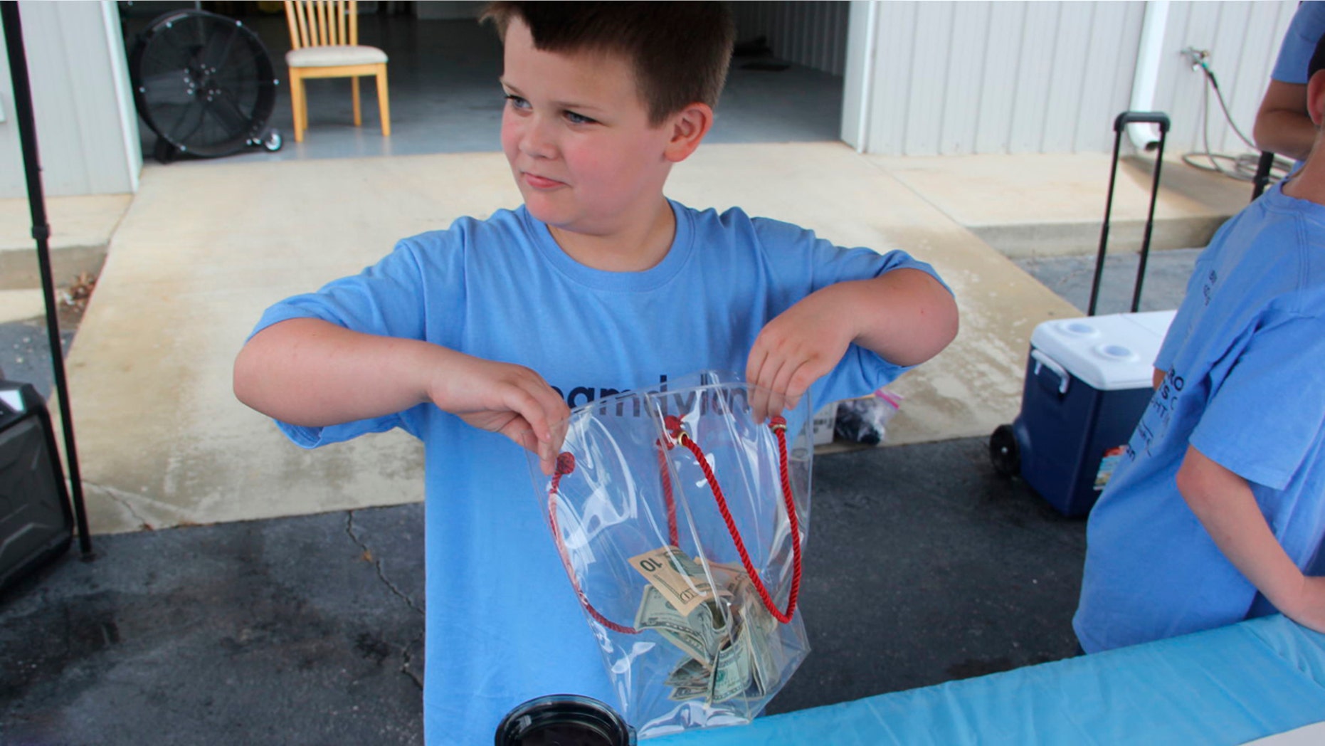 In this Saturday, May 26, 2018, photo, Andrew Emery collects donations at a lemonade stand he set up in Greenwood, S.C., to benefit his baby brother, Dylan. Andrew, the 9-year-old South Carolina boy selling lemonade to help his sick baby brother, has raised nearly $6,000 in two hours. (Adam Benson/The Index-Journal via AP)