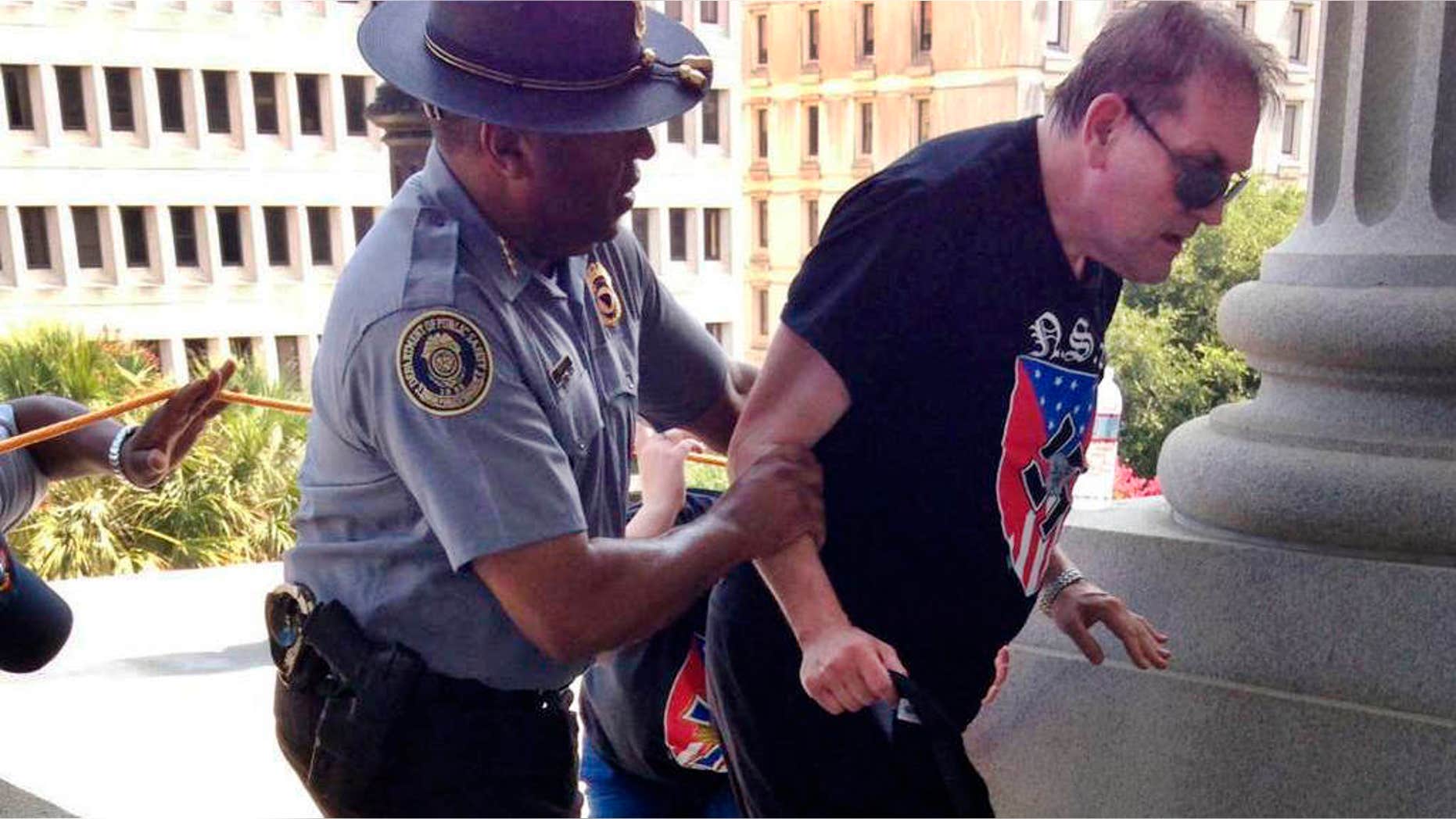 July 18, 2015: In this photo provided by Rob Godfrey, police officer Leroy Smith, left, helps a man wearing National Socialist Movement attire up the stairs during a rally.
