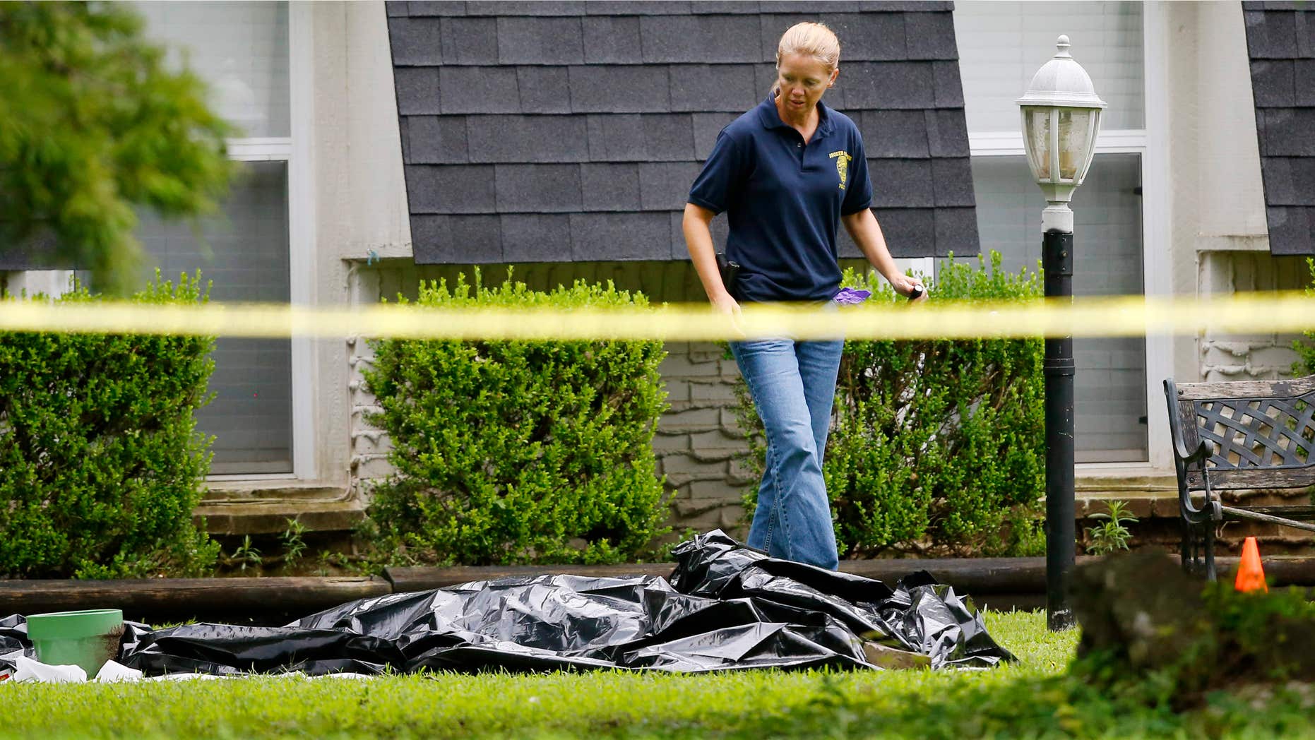 July 23, 2015: An investigator walks past a tarp covering a body in the front yard of a house in Broken Arrow, Okla.
