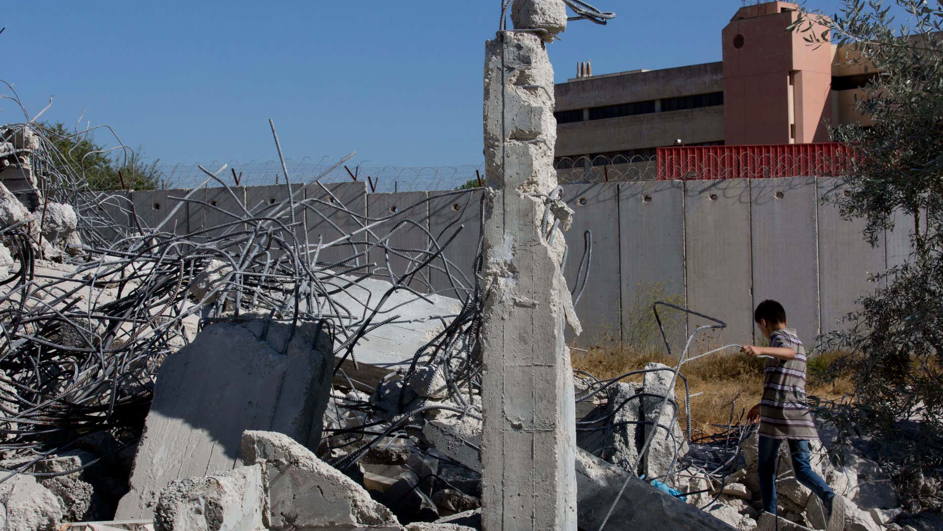 July 26, 2016: A Palestinian boy walks over the rubble of a house that overlooks the Israeli separation barrier, background, and was demolished by the Israeli army, in the West Bank village of Qalandia, near Ramallah.
