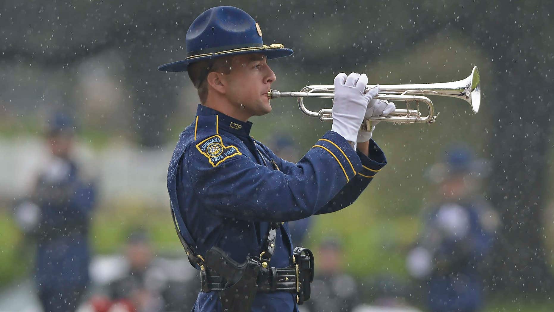 July 25, 2016: A member of the Louisiana State Police Honor Guard plays "Taps" through driving rain during funeral services for Baton Rouge police Cpl. Montrell Jackson in Baton Rouge, La.