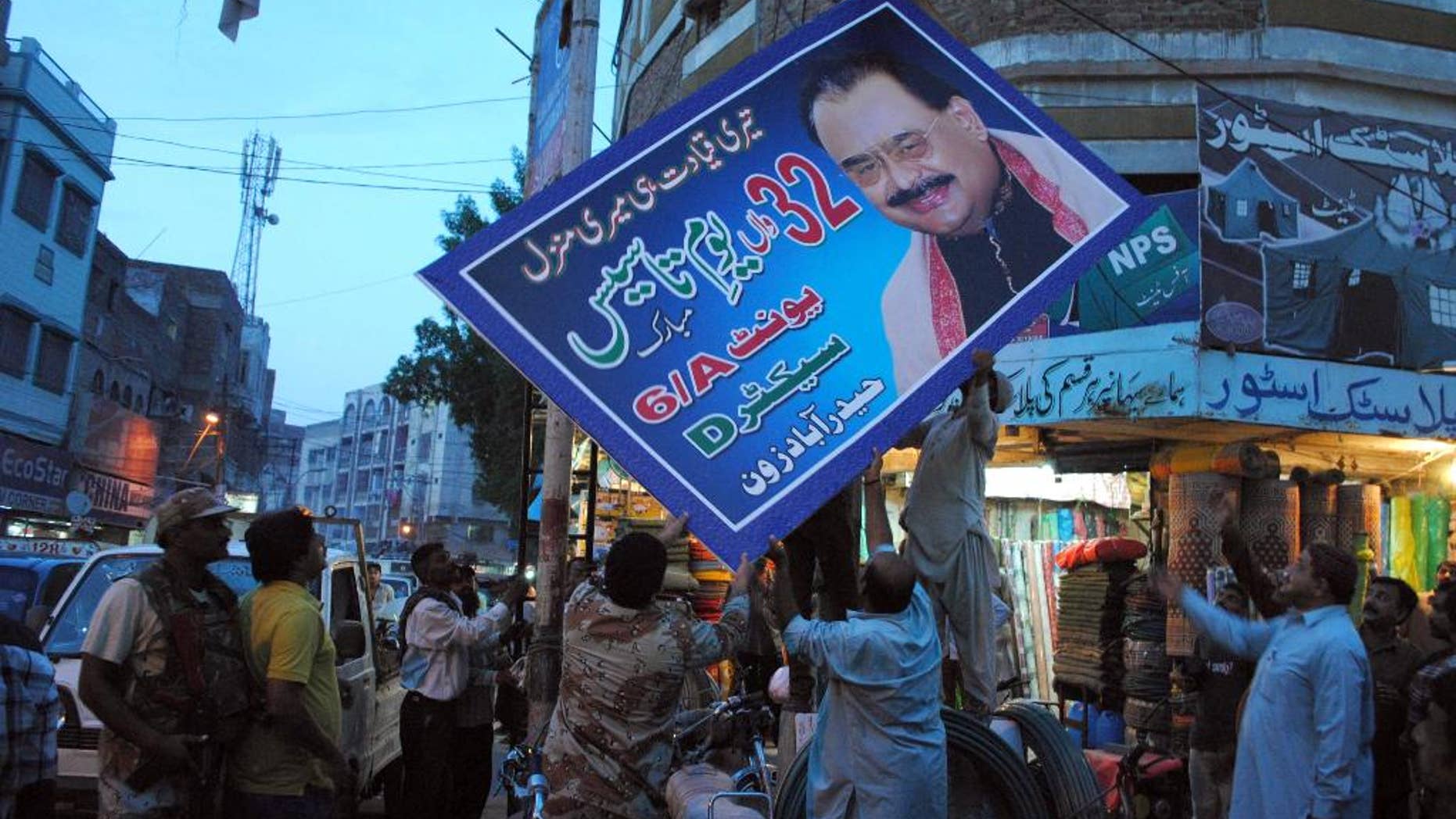FILE - In this Thursday, Aug. 25, 2016 file photo, Pakistani paramilitary forces remove a poster of Altaf Hussain, leader of the Muttahida Qaumi Movement, or MQM, in Hyderabad, Pakistan. Pakistan's Ministry of Interior said it has written a formal request to London to seek legal action against Hussain. A ministry statement says the government sent a dossier on Hussain to U.K. authorities on Tuesday, Aug. 30, 2016, with allegations of inciting violence and disturbing law and order in Pakistan. (AP Photo/Pervez Masih, File)