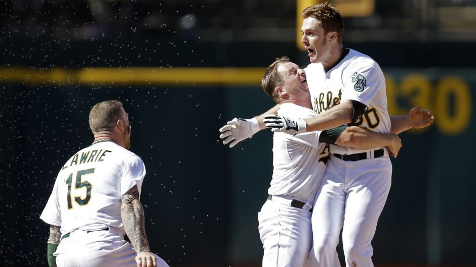 Oakland Athletics' Stephen Vogt, center, lifts Mark Canha after Canha hit the game winning hit in the tenth inning of a baseball game against the Cleveland Indians, Sunday, Aug. 2, 2015, in Oakland, Calif. At left is A's Brett Lawrie (15). The A's won, 2-1.