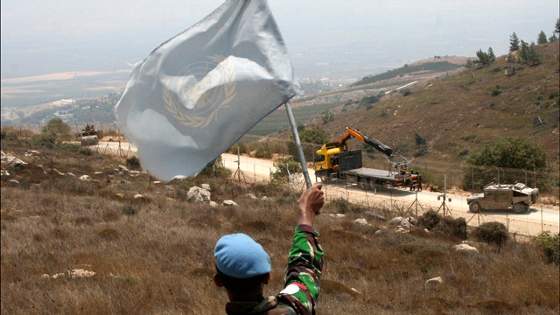 Aug. 3: A UNIFIL peacekeeper waves a U.N. flag as Israeli troops patrol the border in the southern border village of Adaisseh, Lebanon.