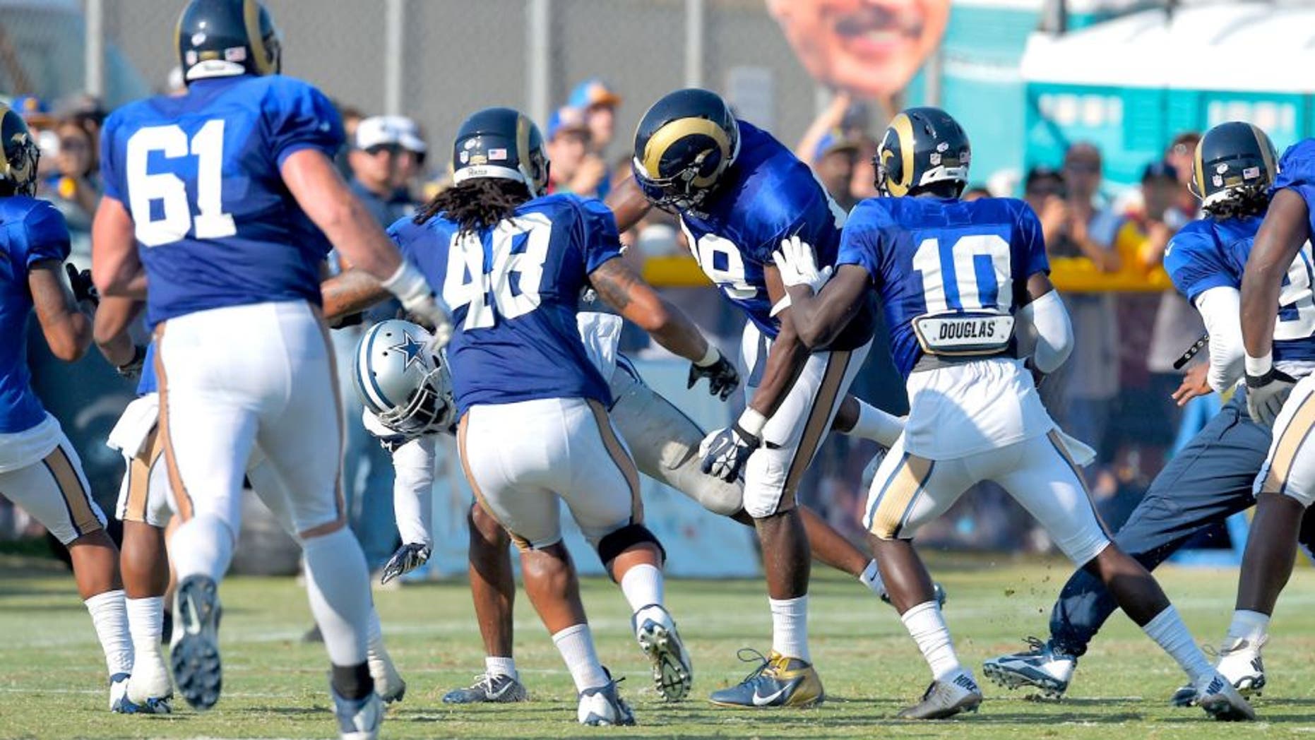 A member of the Dallas Cowboys is thrown to the ground by St. Louis Rams tight end Jared Cook, center, during a scuffle as fans hold up a picture of Rams owner Stan Kroenke during a joint NFL football training camp, Tuesday, Aug. 18, 2015, in Oxnard, Calif. (AP Photo/Mark J. Terrill)