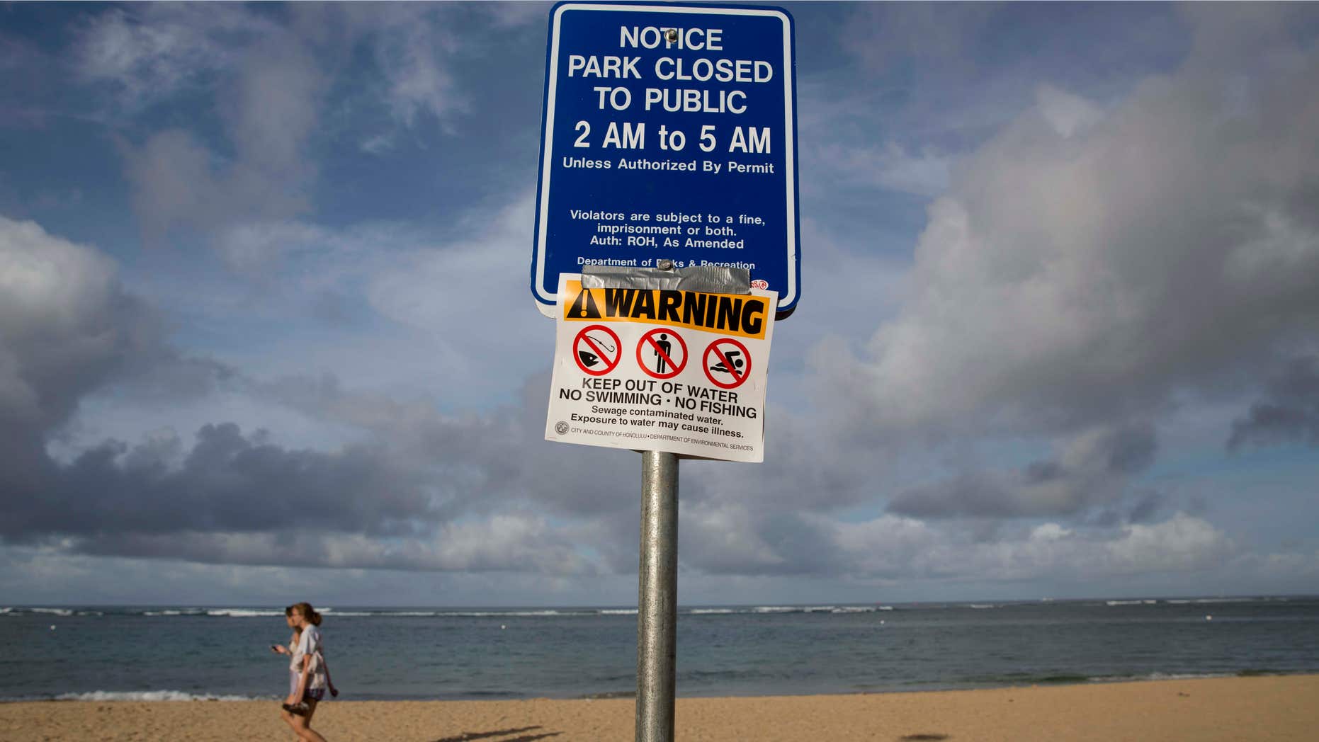 Aug. 25, 2015: Tourists walks near a warning sign posted on Waikiki Beach in Honolulu.