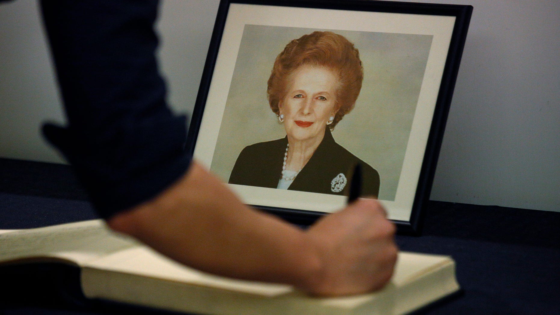 A man signs the condolence book in front of a picture of former British Prime Minister Margaret Thatcher at the British Consulate in Hong Kong Tuesday, April. 9, 2013.