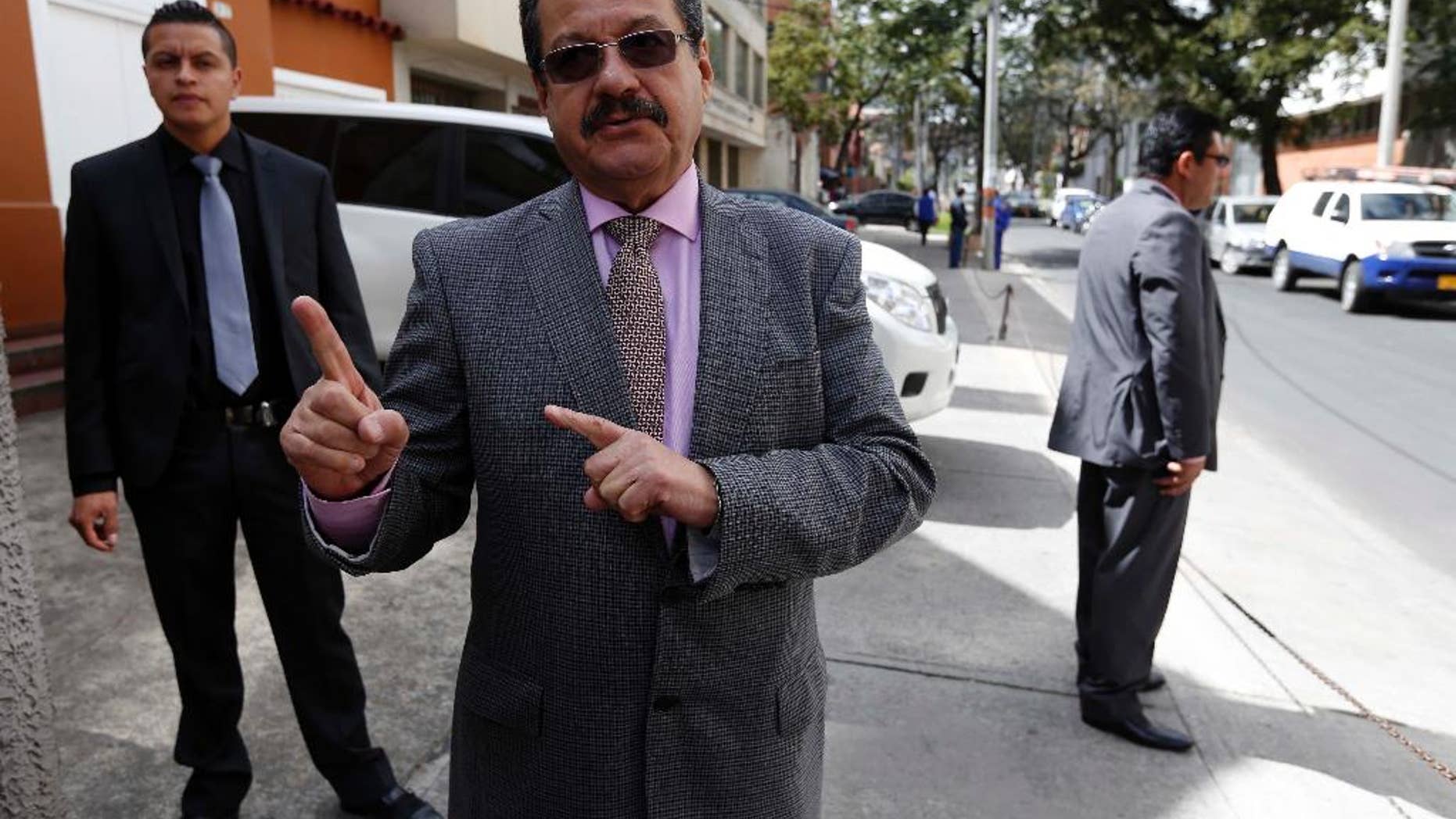In this Sept. 30, 2014 photo, Carlos Lozano, director of the Colombian Communist Party's weekly "Voz," speaks to The Associated Press as two bodyguards watch over him, outside his office in Bogota, Colombia. Lozano, a Communist politician who has been an intermediary to the FARC, says the government isn’t doing enough to convince the rebels they will be safer on the streets than they are on the battlefield. (AP Photo/Fernando Vergara)