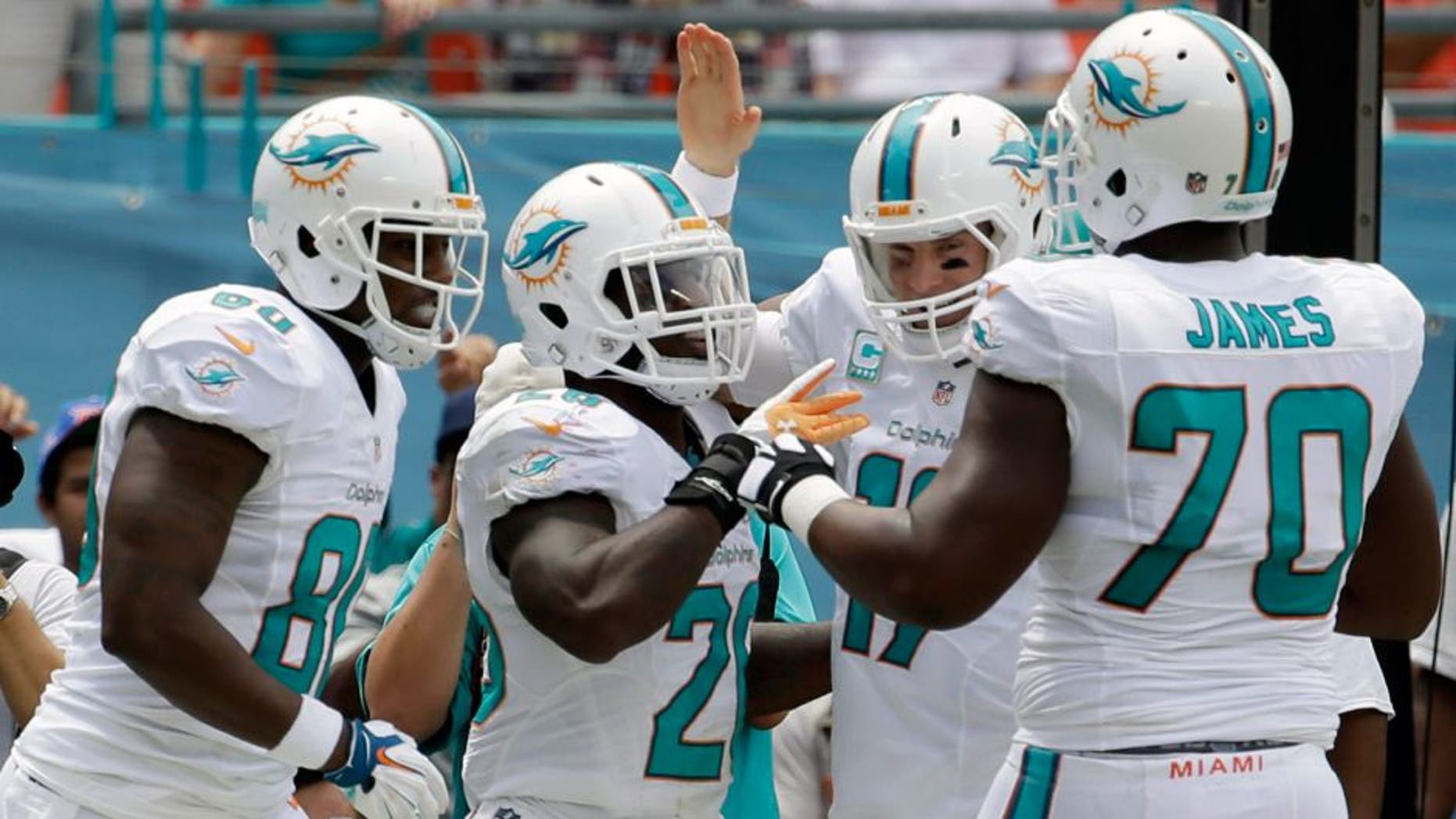 Miami Dolphins running back Lamar Miller, second from left, is congratulated by tight end Dion Sims, left, quarterback Ryan Tannehill, second from right, and offensive tackle Ja'Wuan James (70) after Miller scored a touchdown during the first half of an NFL football game against the New England Patriots, Sunday, Sept. 7, 2014, in Miami Gardens, Fla. (AP Photo/Lynne Sladky)