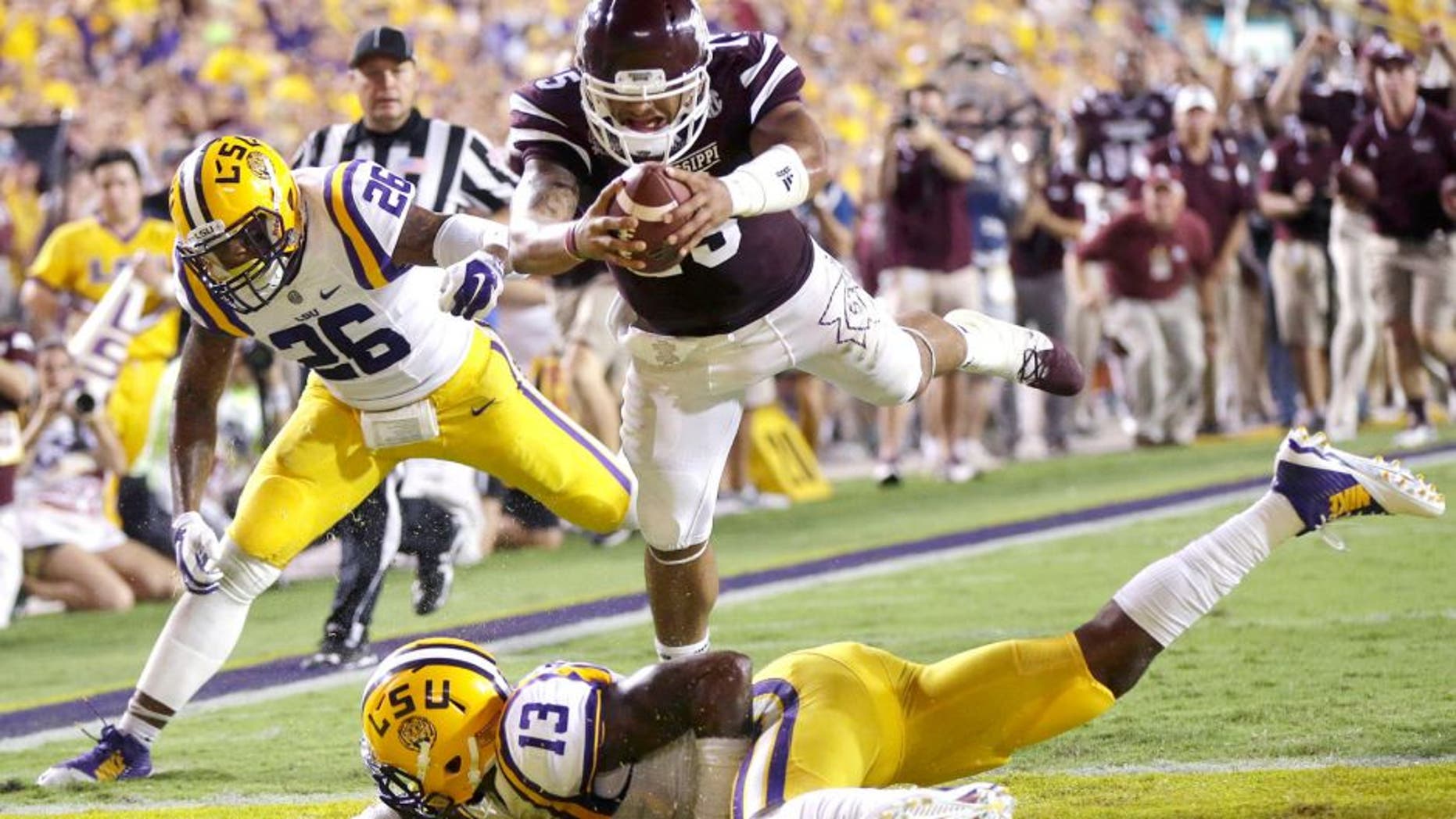 Mississippi State quarterback Dak Prescott (15) dives into the end zone over LSU cornerback Dwayne Thomas (13) and safety Ronald Martin (26) on a 56 yard touchdown run in the second half of an NCAA college football game in Baton Rouge, La., Saturday, Sept. 20, 2014. (AP Photo/Gerald Herbert)