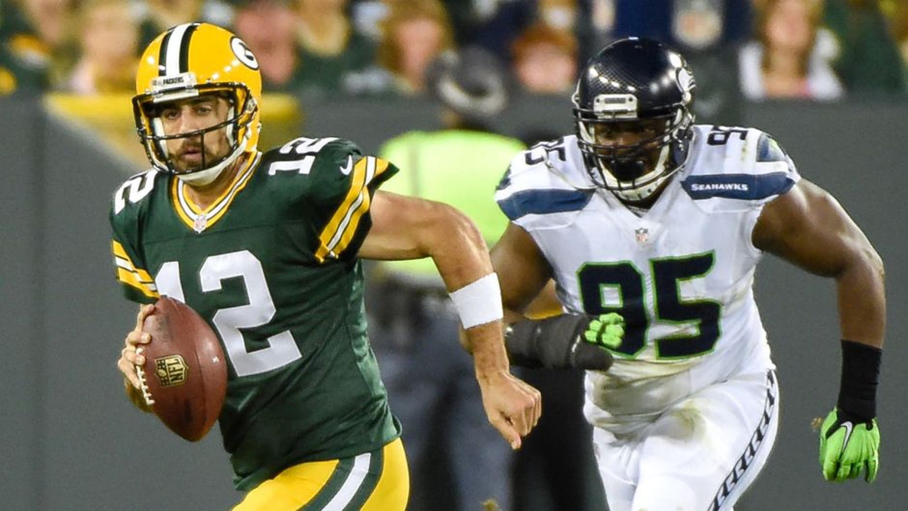 Sep 20, 2015; Green Bay, WI, USA; Green Bay Packers quarterback Aaron Rodgers (12) scrambles away from Seattle Seahawks defensive end Demarcus Dobbs (95) in the second quarter at Lambeau Field. Mandatory Credit: Benny Sieu-USA TODAY Sports