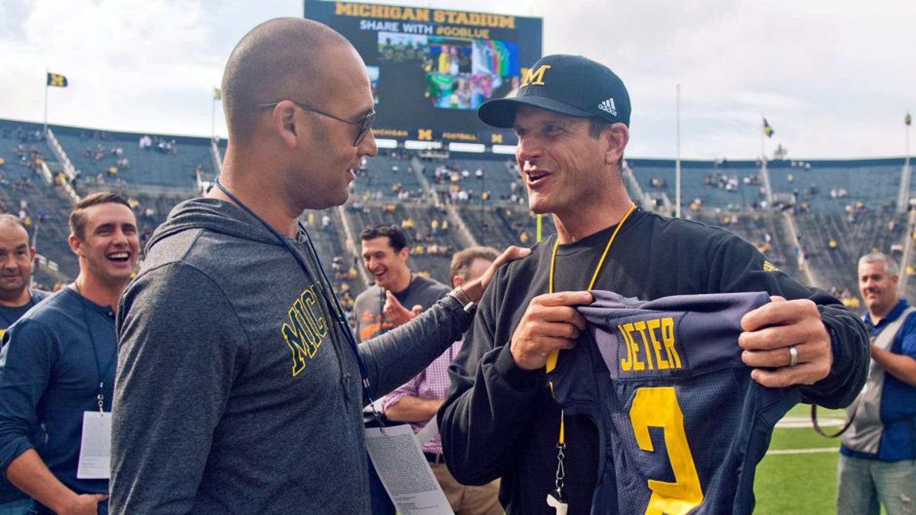 Former New York Yankees baseball player Derek Jeter, left, receives a jersey with his name an No, 2 from Michigan head coach Jim Harbaugh, right, before Michgan's NCAA college football game against BYU in Ann Arbor, Mich., Saturday, Sept. 26, 2015. Jeter graduated high school in Kalamazoo, Mich. and was offered a scholarship to play baseball for Michigan. (AP Photo/Tony Ding)
