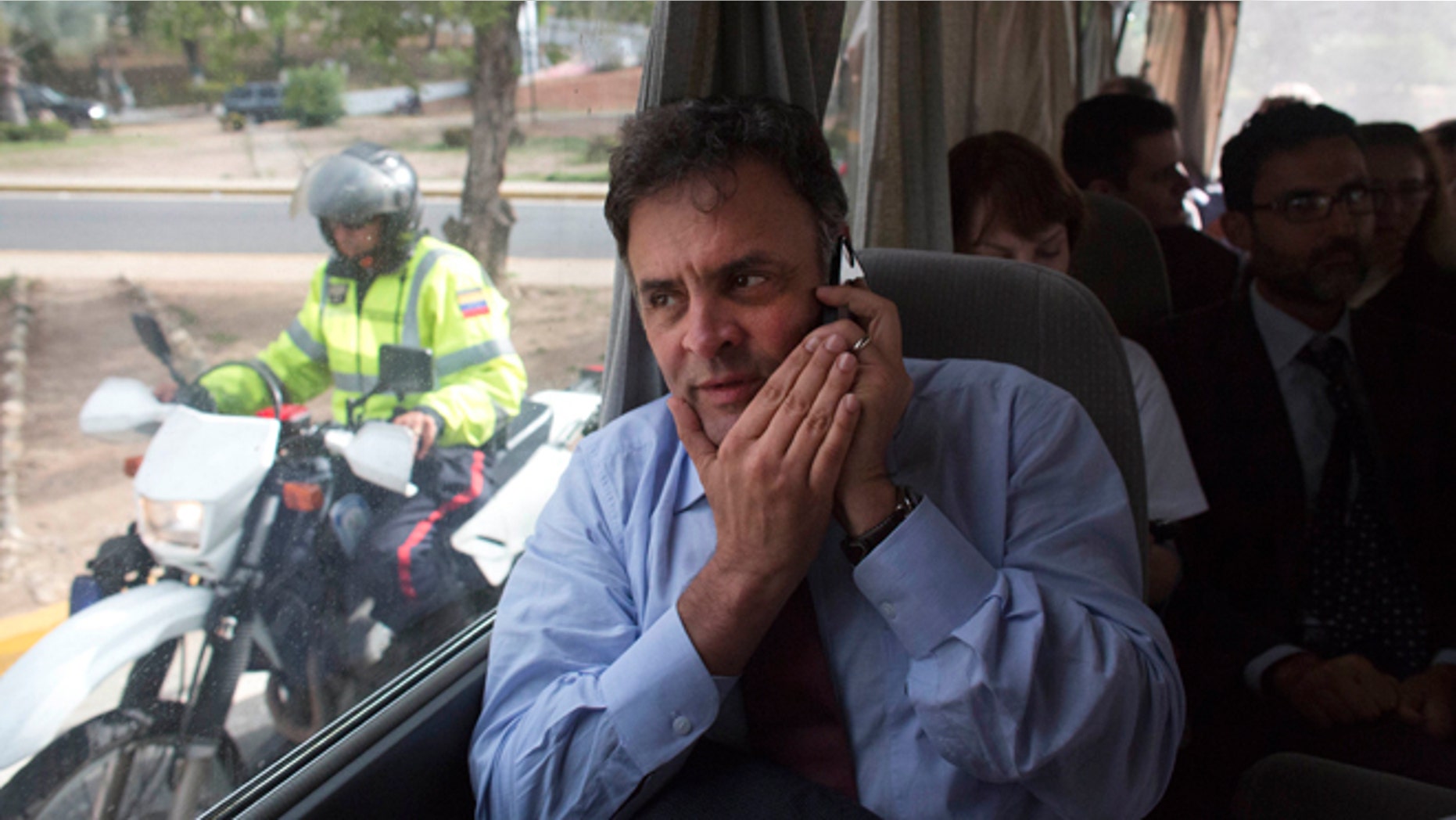 Brazilian Senator Aecio Neves speaks on his cell phone as he rides in a van with other Brazilian senators, escorted by Bolivarian Police on motorcycles, after departing the airport in La Guaira, Venezuela, Thursday, June 18, 2015. The group of Brazilian senators failed to reach the capital city of Caracas twice, due to traffic caused by a demonstration and road maintenance. The delegation had traveled to Venezuela to meet with members of Venezuela's opposition but returned to the airport to fly back to Brazil. (AP Photo/Ariana Cubillos)
