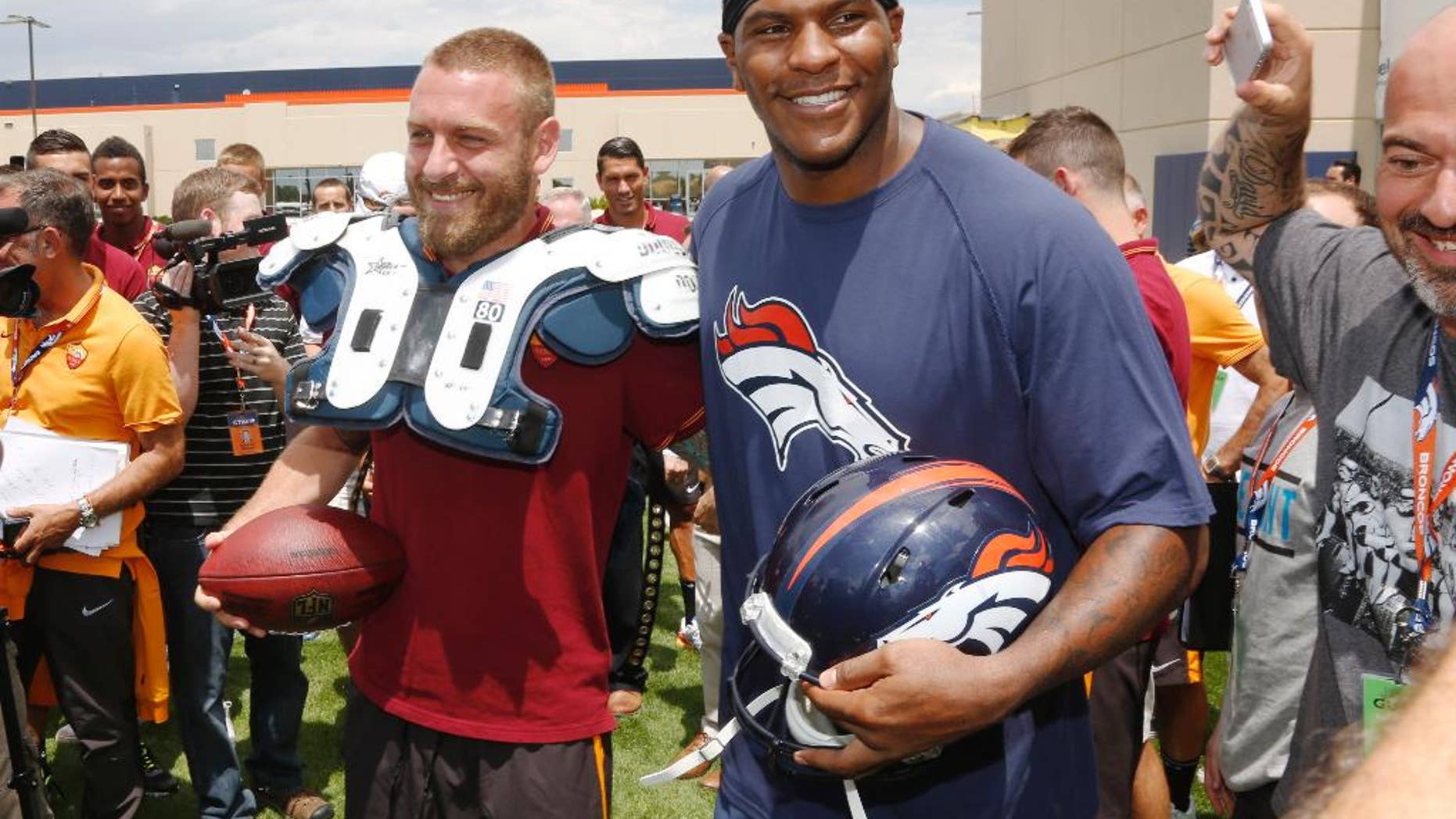 AS Roma player Daniele De Rossi, left, tries on the shoulder pads of Denver Broncos tight end Julius Thomas as members of the Italian soccer team meet Broncos players after the Broncos' NFL football training camp session in Englewood, Colo., on Friday, July 25, 2014. AS Roma is in Denver to face Manchester United on Saturday. (AP Photo)