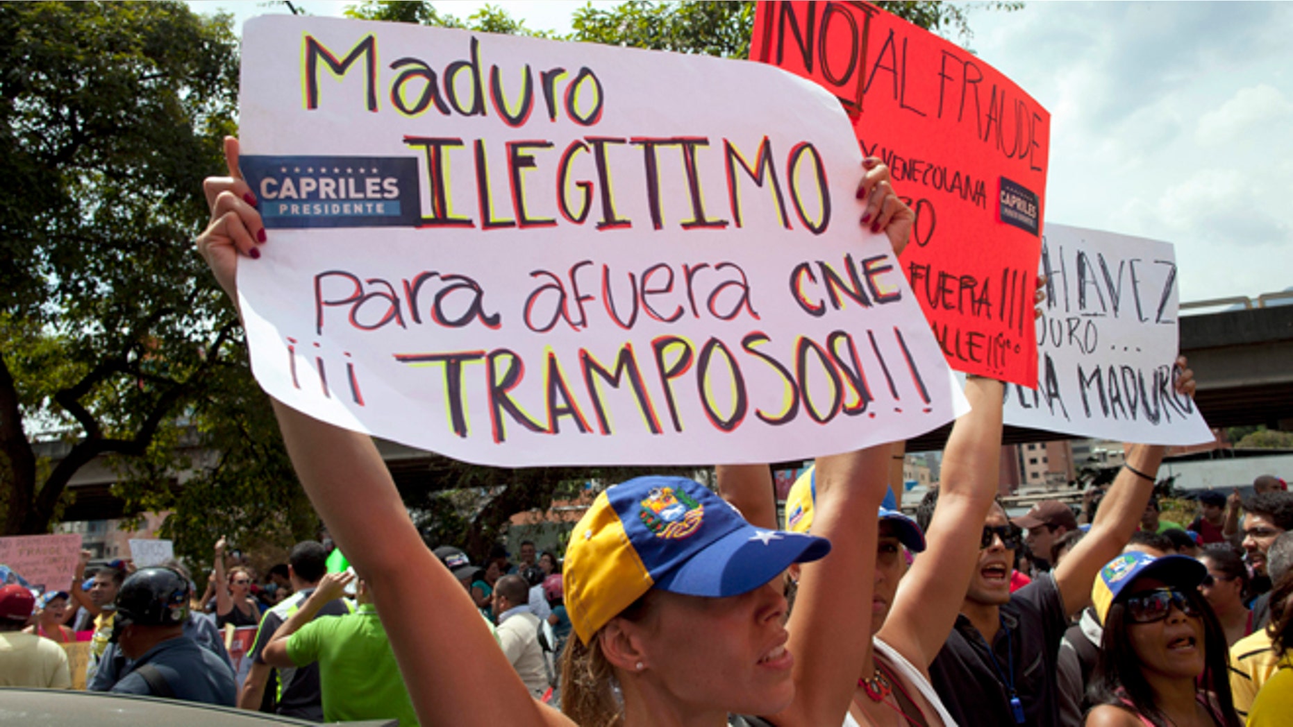 Opposition supporters protest the official results of the presidential election holding a sign that reads in Spanish "Maduro, illegitimate, get out CNE.