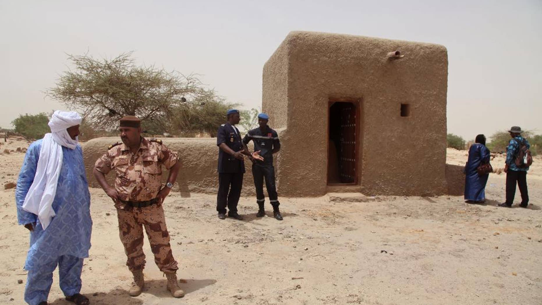 FILE - In this file photo taken Saturday, July 18, 2015, people attending a ceremony stand near a mausoleum, right, that was restored in Timbuktu, Mali after the 14 mausoleums in Mali’s northern historic city that had been destroyed by Islamic extremists in 2012 have been restored. An alleged Islamic extremist charged with involvement in the destruction of religious buildings has been arrested and was sent to the International Criminal Court early Saturday, Sept. 26, 2015 to face justice. (AP Photo/Baba Ahmed, File)