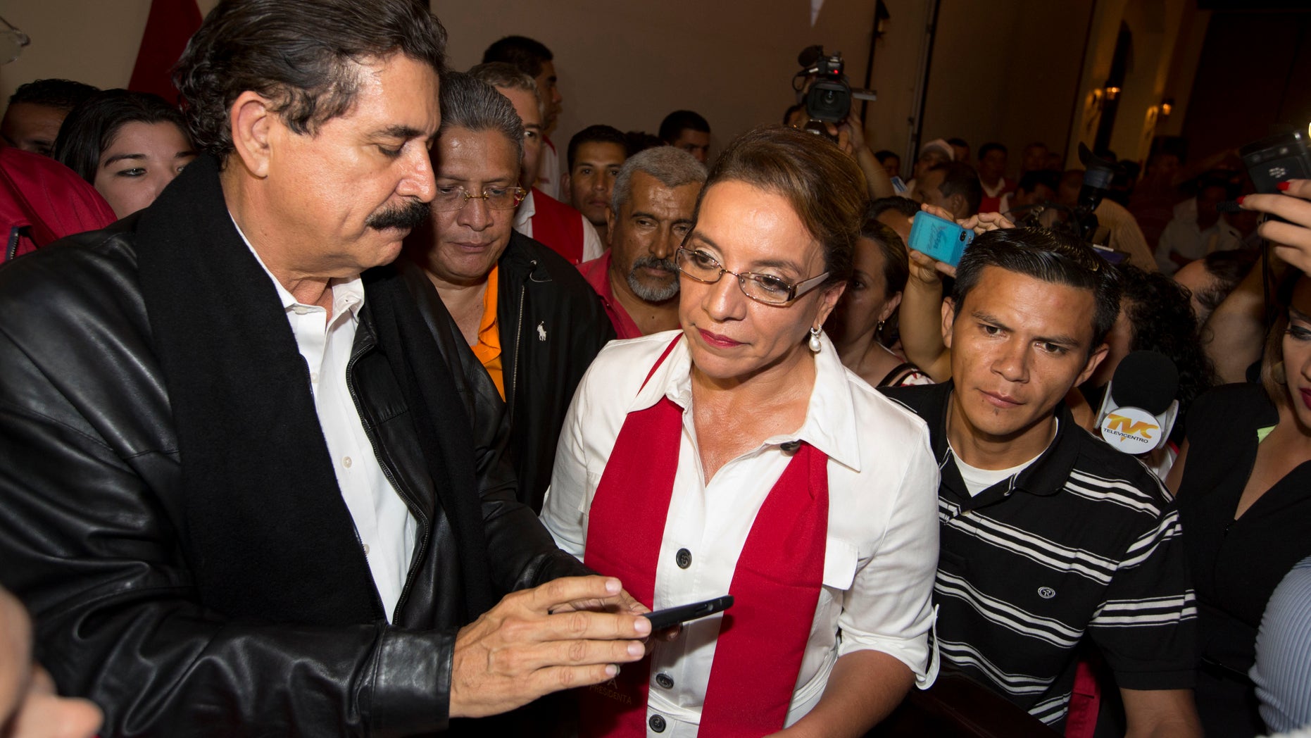 Free Party presidential candidate Xiomara Castro, center, and her husband, ousted President Manuel Zelaya, left, check information on his cell phone before the announcement of official election results in Tegucigalpa, Honduras, Sunday, Nov. 24, 2013. Hondurans cast ballots for a new president Sunday in a country reeling from violence, poverty and the legacy of a 2009 coup that ousted Zelaya. (AP Photo/Moises Castillo)
