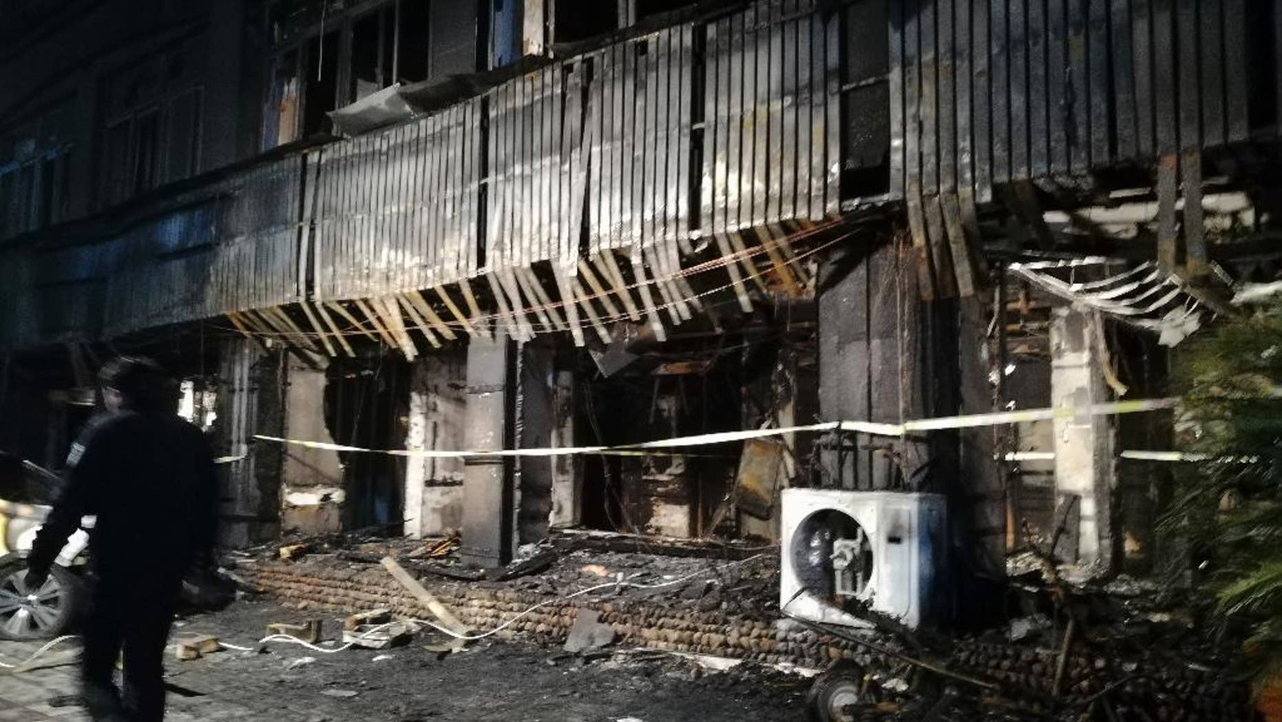 In this photo released by Xinhua News Agency, a man walks past the Zuxintang Foot Massage Parlor damaged by a fire in Tiantai County, east China's Zhejiang Province, Monday, Feb. 6, 2017. The fire at the massage parlor on Sunday killed and injured dozens of people, state media reported. (Wang Junlu/Xinhua via AP)