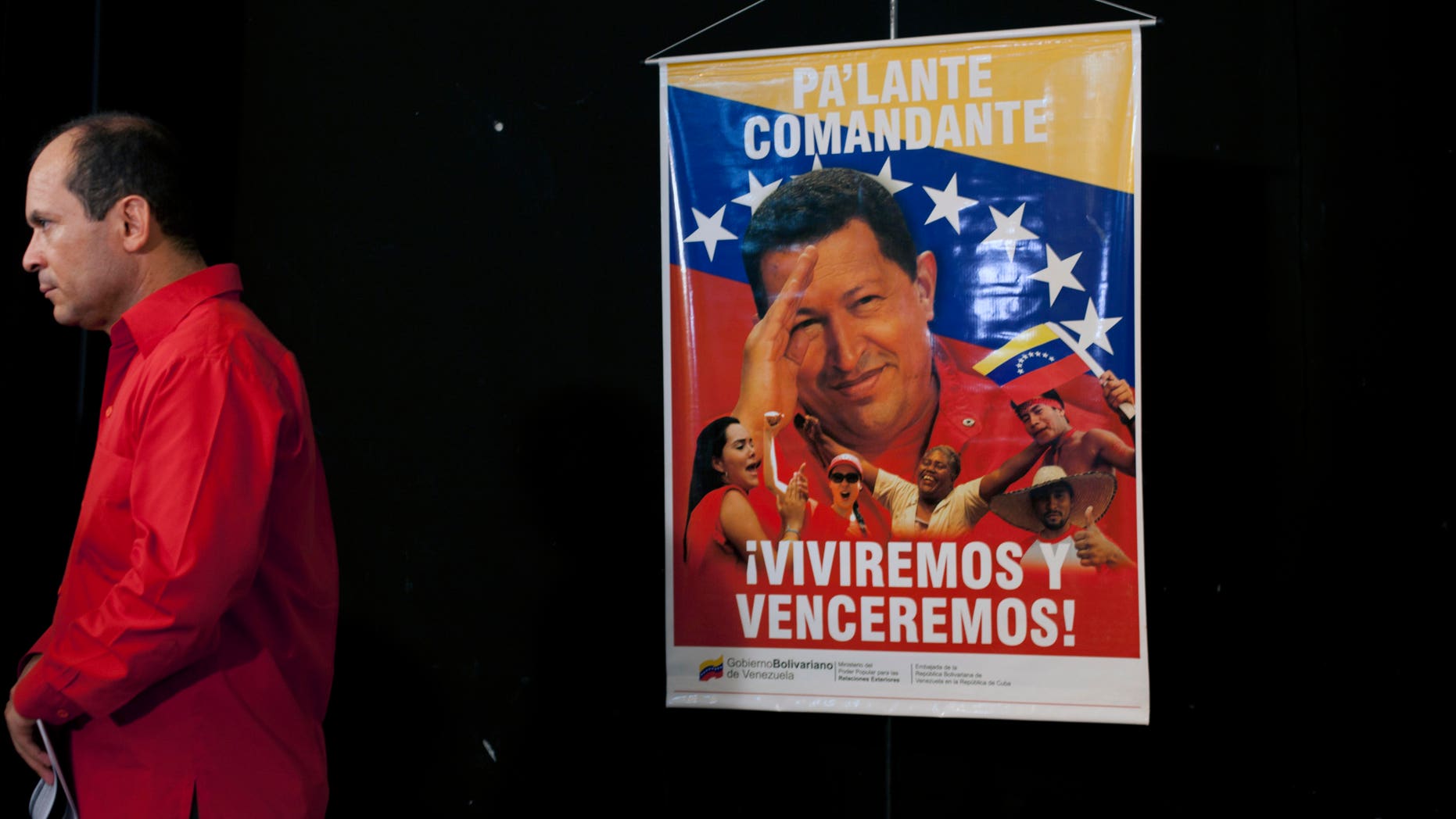 A poster of Venezuela's President Hugo Chavez that reads "Move forward commander, we will live and overcome" hangs as Venezuela's ambassador to Cuba Edgardo Antonio Ramirez stands by after a press conference by Cuban artists and intellectuals to show support for Chavez in Havana, Cuba, Monday, Jan. 7, 2013. Chavez hasn't spoken or appeared publicly since his Dec. 11 operation in Cuba, his fourth surgery for an undisclosed type of pelvic cancer. Speculation about the leader's condition has grown since the operation. (AP Photo/Ramon Espinosa)