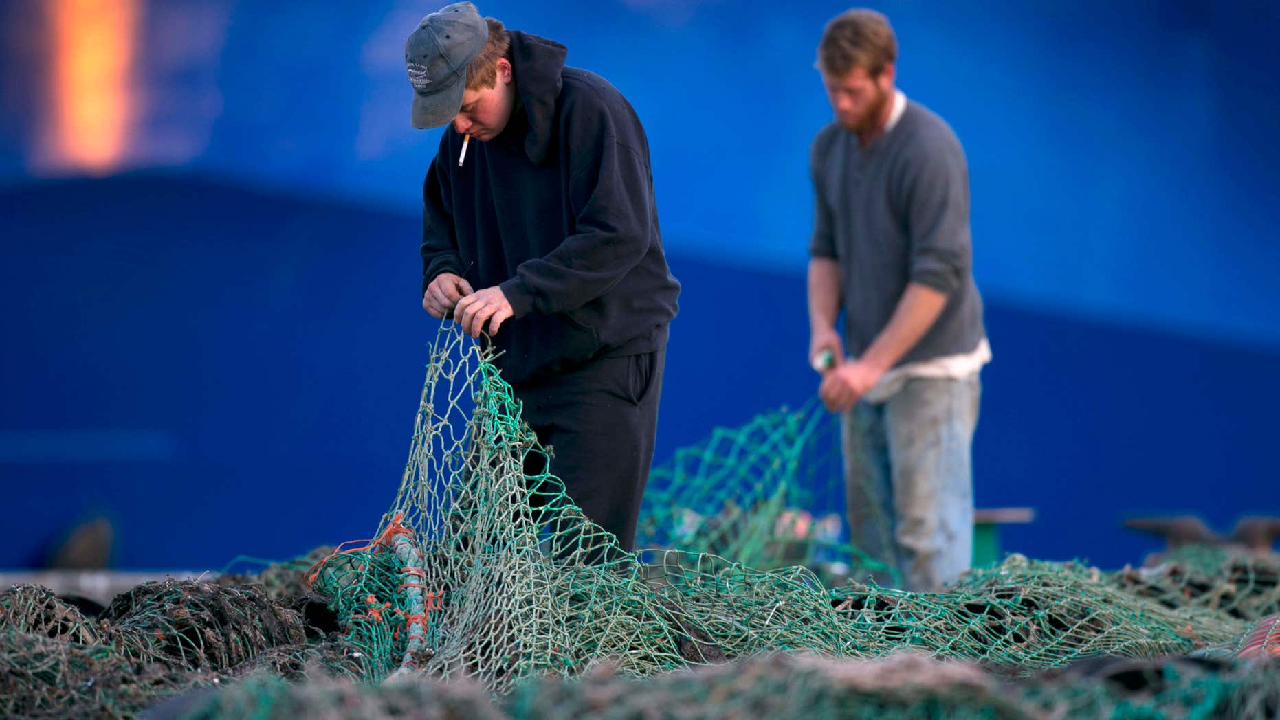 FILE - In this Nov. 15, 2013 file photo, fishermen Ed Stewart, left, and Tannis Goodsen mend groundfishing nets on Merrill Wharf in Portland, Maine.