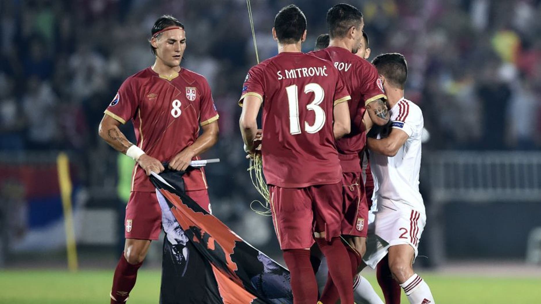 Serbia's midfielder Nemanja Gudelj (L) holds a flag with Albanian national symbols pulled down by Serbia's defender Stefan Mitrovic (C) from a remotely operated drone flown over the pitch during the EURO 2016 group I football match between Serbia and Albania in Belgrade on October 14, 2014. AFP PHOTO / ANDREJ ISAKOVIC (Photo credit should read ANDREJ ISAKOVIC/AFP/Getty Images)