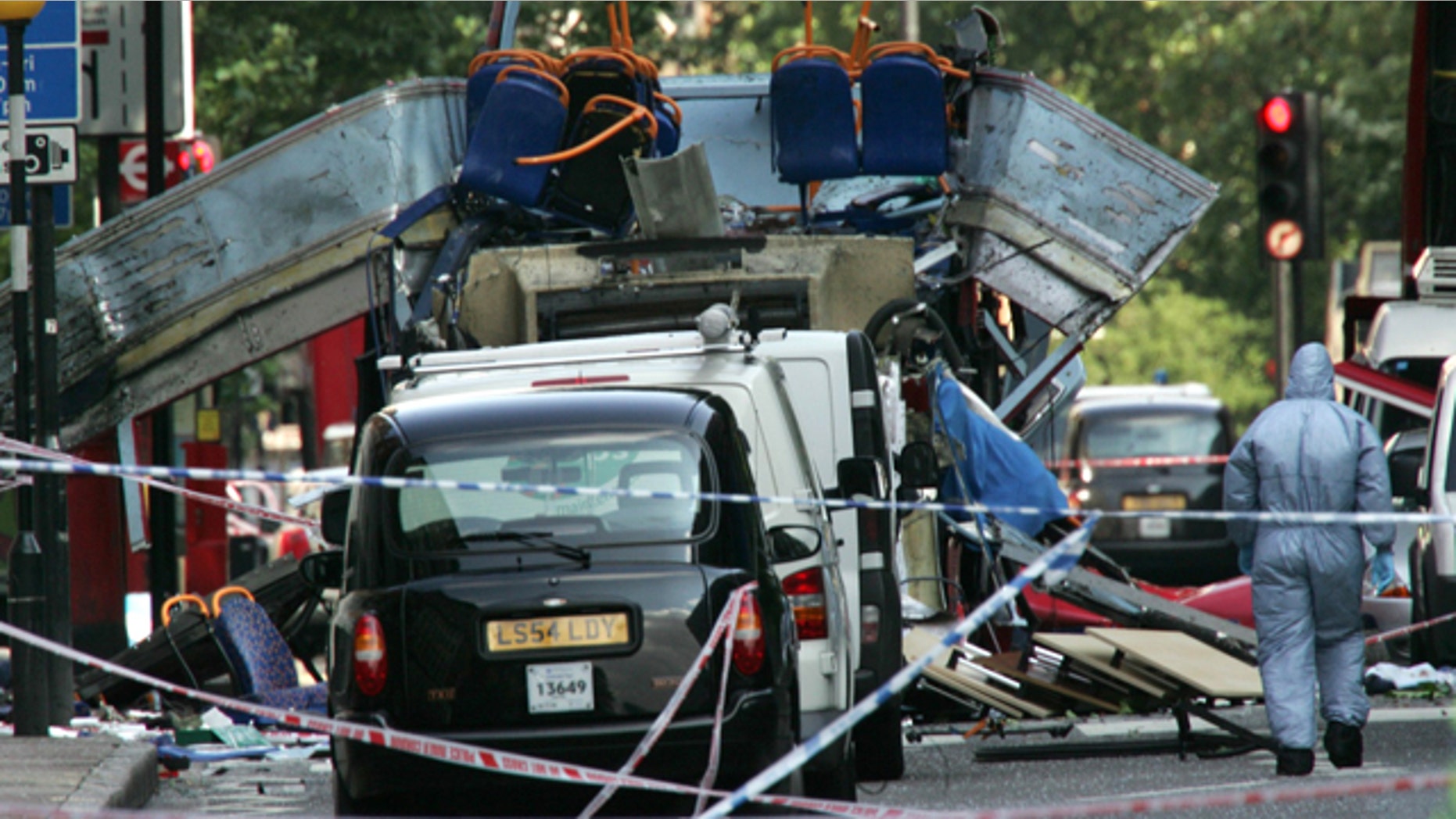 In this July 7, 2005 file photo, a forensic officer walks next to the wreckage of a double decker bus with its top blown off and damaged cars scattered on the road at Tavistock Square in central London.