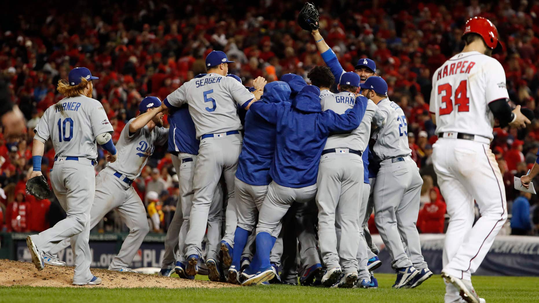 As Washington Nationals' Bryce Harper (34) walks from the field, the Los Angeles Dodgers celebrate a 4-3 win in Game 5 of a baseball National League Division Series, at Nationals Park early Friday, Oct. 14, 2016, in Washington.
