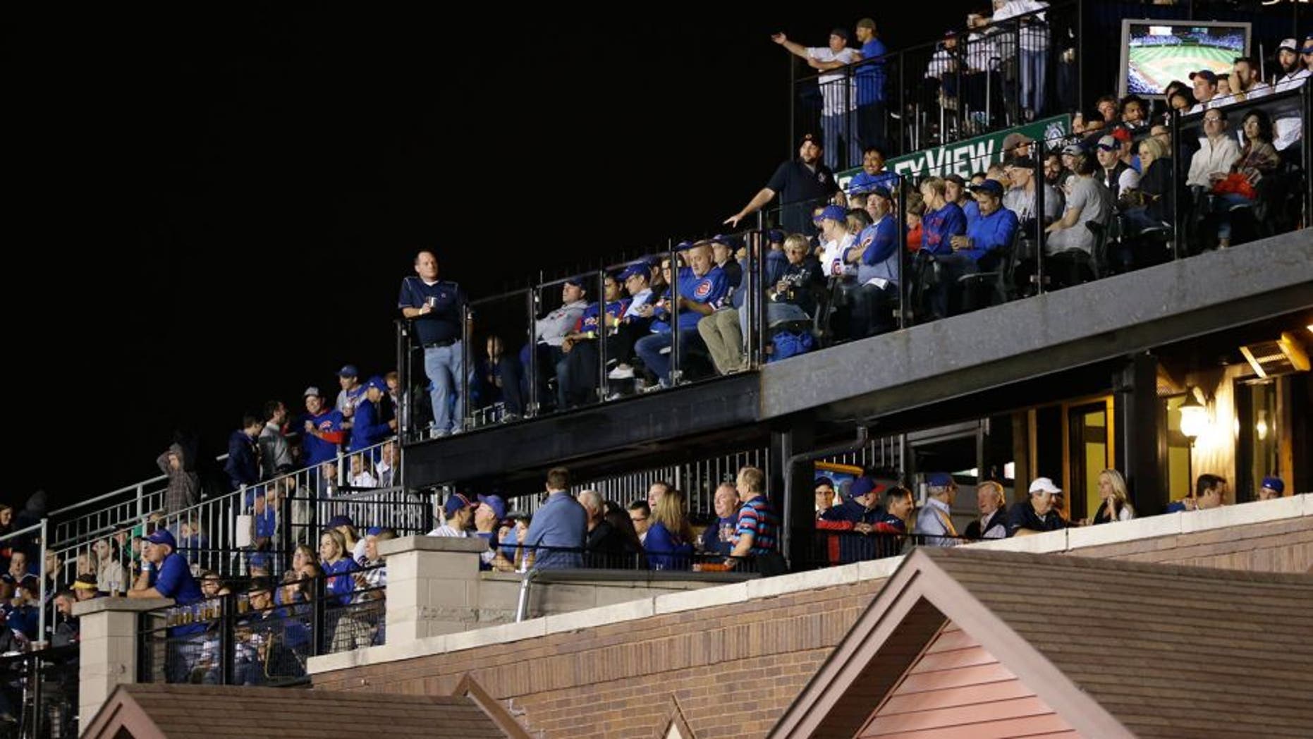 In this Oct. 20, 2015 photo, fans watch Game 3 of the National League baseball championship series between the Chicago Cubs and the New York Mets in Chicago, from the rooftop deck across the street beyond Wrigley Field's ivy-covered wall. With the massive Jumbotron now standing between the rooftop bleachers and the field, the 2015 postseason is the first for the Cubs since the team sliced into the views from the rooftops - one of the fabled experiences at this venerable old ballpark, and one in serious danger of going away for good. (AP Photo/David Goldman)
