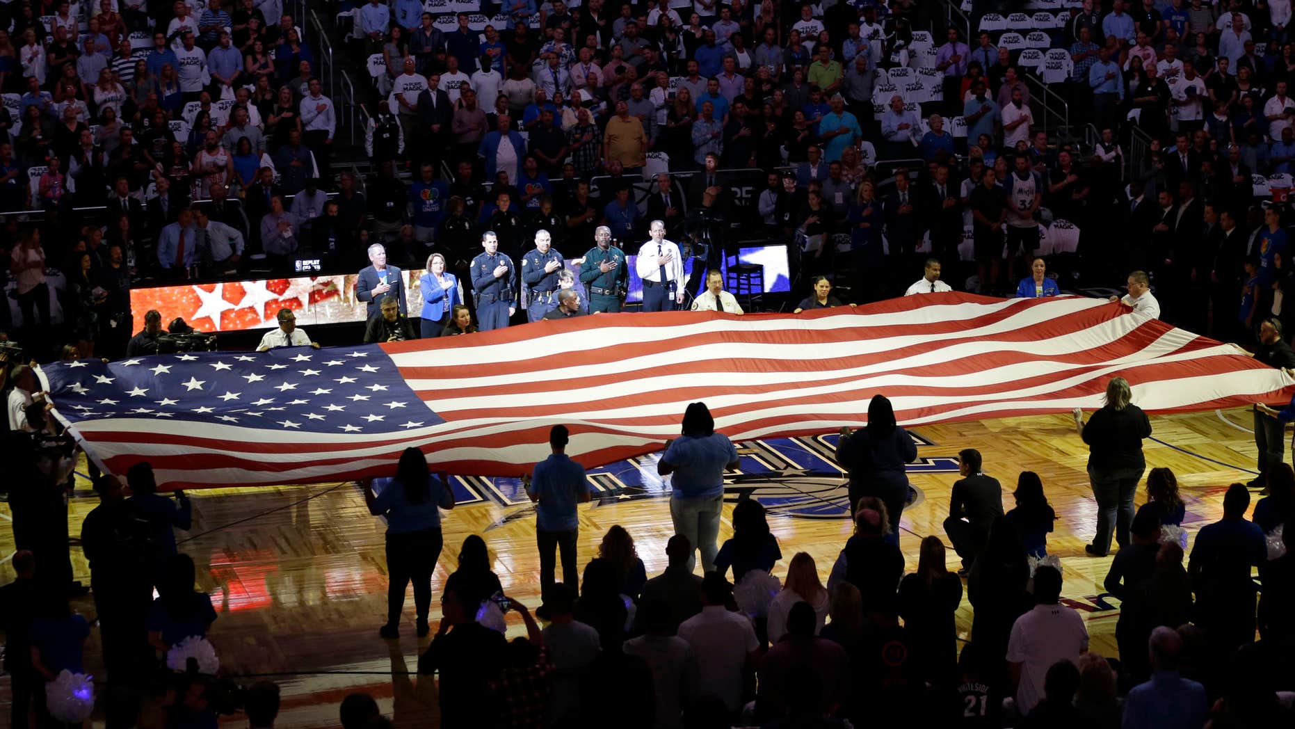 First responders hold a flag on the court as the national anthem is played during a tribute to the victims of the Pulse nightclub shooting prior to an NBA basketball game between the Orlando Magic and the Miami Heat, Wednesday, Oct. 26, 2016, in Orlando, Fla.