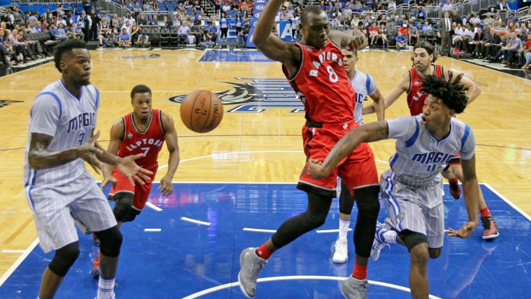 Orlando Magic guard Elfrid Payton (4) passes the ball around Toronto Raptors forward Bismack Biyombo (8) to center Dewayne Dedmon, left, during the first half of an NBA basketball game, Friday, Nov. 6, 2015, in Orlando, Fla. (AP Photo/John Raoux)