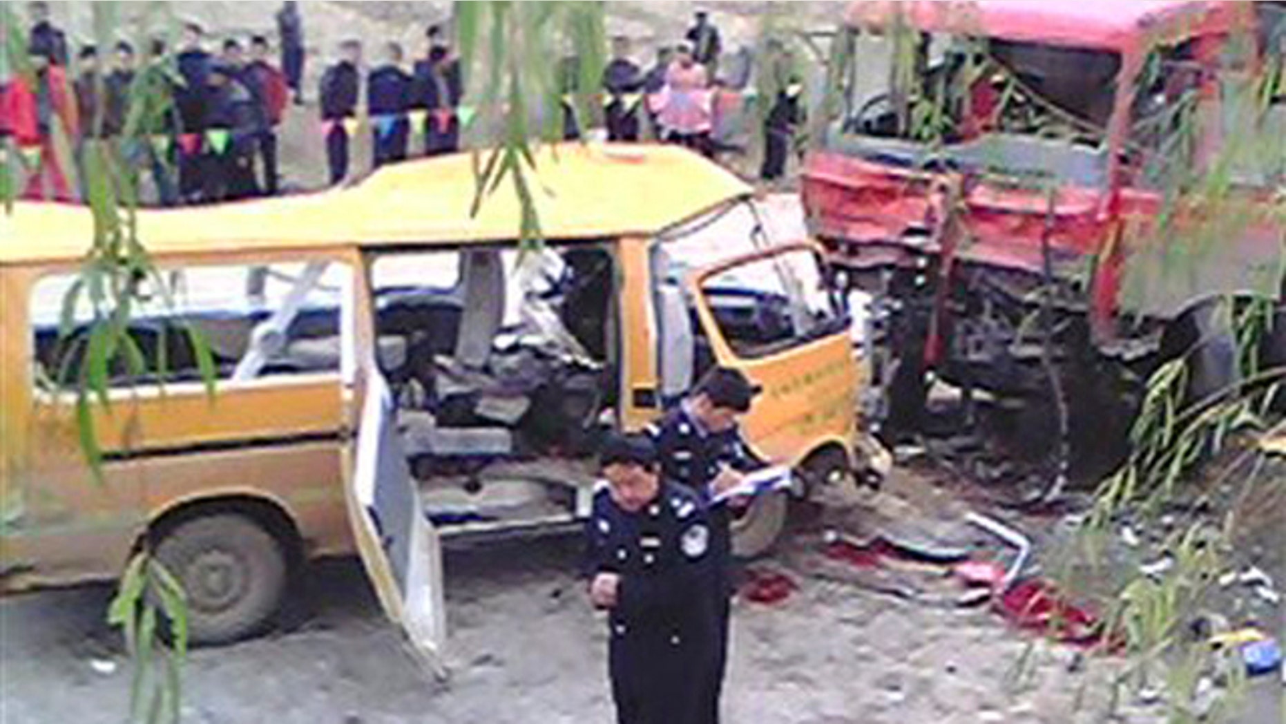 November 16, 2011: In this photo taken on a mobile phone, two police officers, front, investigate at the accident scene where a kindergarten minibus, left, collided head-on with a truck loaded with coal, right, on a road at Yu Linzi township in Qingyang.