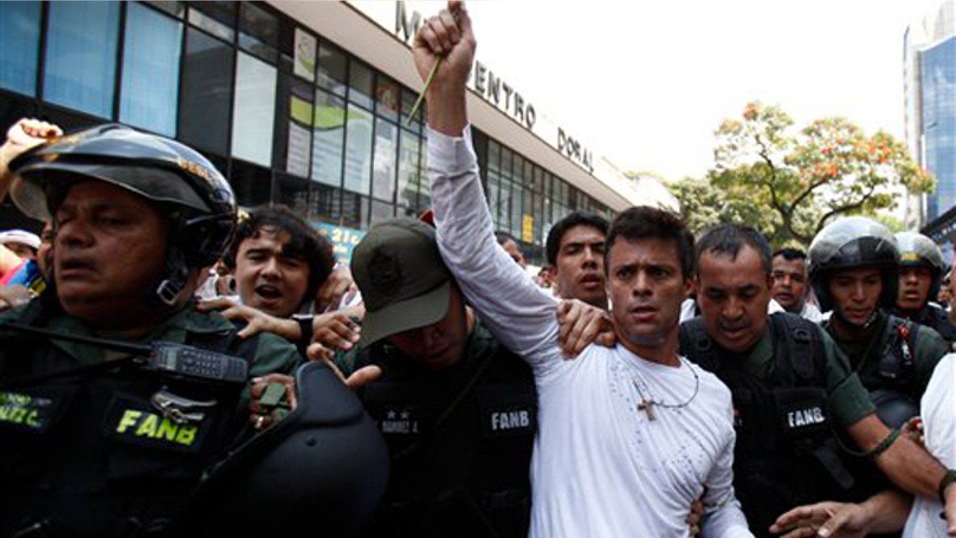 Opposition leader Leopoldo Lopez, dressed in white and holding up a flower stem, is taken into custody by Bolivarian National Guards, in Caracas, Venezuela, Tuesday, Feb 18, 2014. Lopez re-emerged from days of hiding to address an anti-government demonstration and then he turned himself in to authorities Tuesday. Speaking to some 5,000 supporters with a megaphone, Lopez said that he doesn't fear going to jail to defend his beliefs and constitutional right to peacefully protest against President Nicolas Maduro. (AP Photo/Alejandro Cegarra)