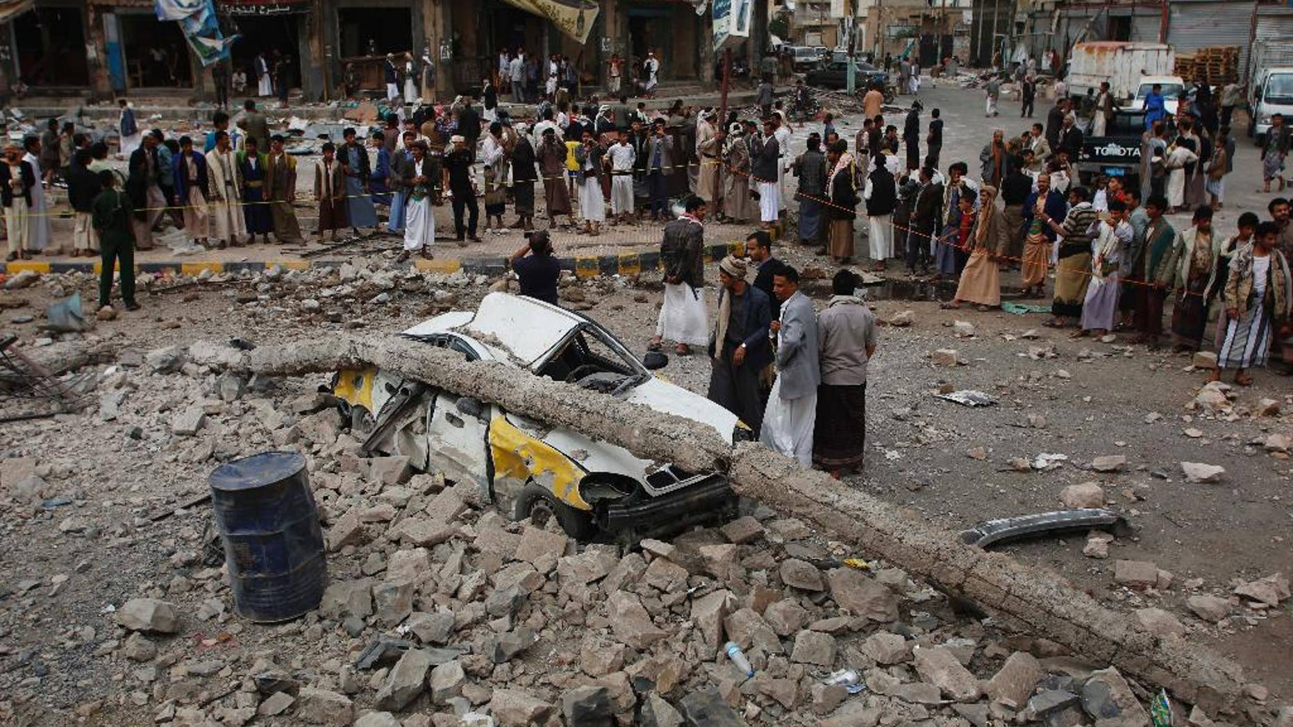 People stand near a vehicle destroyed following airstrikes by the Saudi-led coalition in Sanaa, Yemen, Tuesday, July 14, 2015. The coalition has been targeting the Iran-allied Houthis since March in a bid to stop their power grab across the country. Yemeni forces battling the Shiite rebels in the country's south said they took control on Tuesday of the airport in the strategic port city of Aden. (AP Photo/Hani Mohammed)
