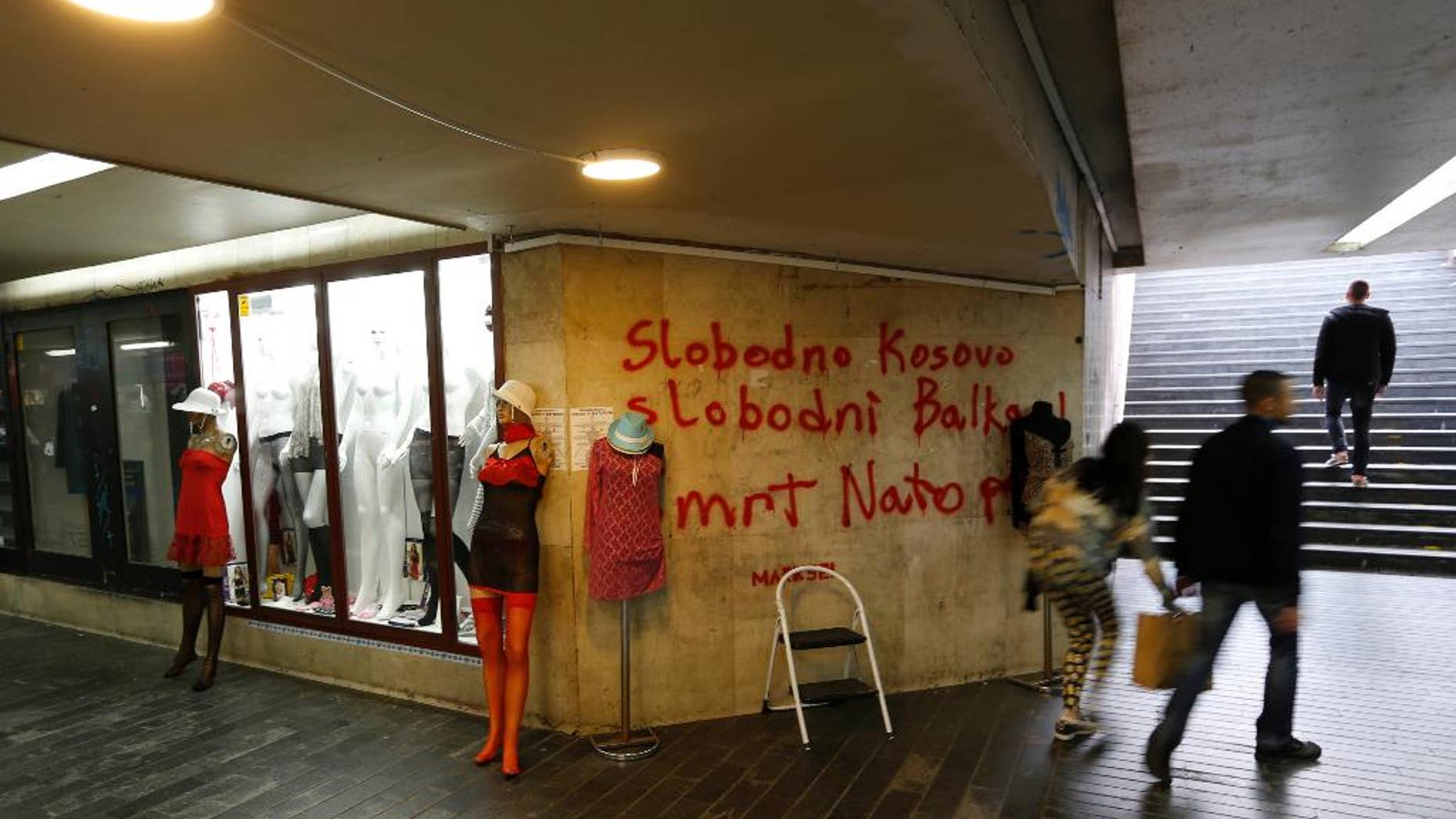 FILE - In this Tuesday April 4, 2017 file photo, people pass through an underground passage with graffiti on the wall that reads: "Free Kosovo, Free Balkan, Death for NATO", in Belgrade, Serbia. The small Adriatic state of Montenegro is set to formally approve becoming a member of NATO, a historic step for the Balkan country that has been split in loyalties to the West and traditional ally Russia. (AP Photo/Darko Vojinovic, File)