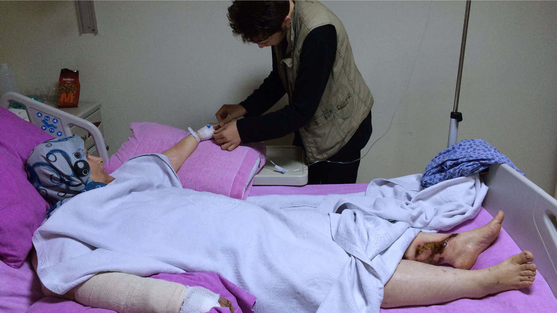 FILE - In this Oct. 24, 2015, file phot taken with a mobile phone, a Syrian boy Abdulhamid Khanfoura, background, helps his wounded mother Zahra Khanfoura, who was burned by a Russian airstrike that hit her house in the central Syrian village of Habeet, as she lies on her hospital bed in the southern city of Kadirli, Turkey.
