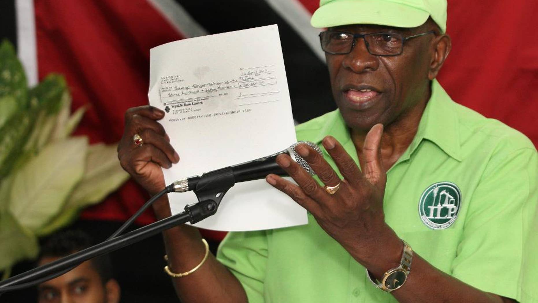 FILE - In this June 3, 2015, file photo, former FIFA vice president Jack Warner hold a copy of a check while he speaks at a political rally in Marabella, Trinidad and Tobago. Trinidad and Tobago’s attorney general has signed documents on Monday, Sept. 21, 2015, that pave the way for U.S. extradition proceedings against Warner. The former FIFA vice president is resisting extradition on U.S. charges of racketeering, wire fraud and money laundering in the FIFA corruption case. (Photo/Anthony Harris, File)