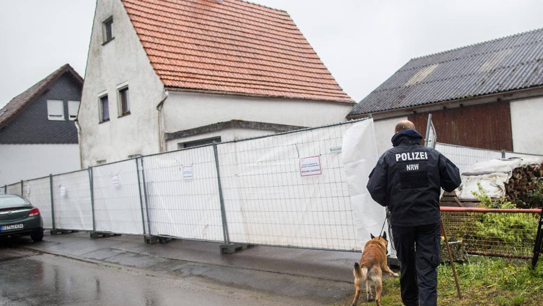FILE - This is a Tuesday, May 3, 2016 file photo of a police officer with a dog as they pass by a house outside Hoexter, western Germany. German police say they have identified at least four women who survived abuse in the home of a couple suspected of killing two other women. Police said Monday May 9, 2016 that they have contacted the survivors, including a woman from the Berlin area who told investigators she was imprisoned for about three months in the house near the western town of Hoexter. (Marcel Kusch/dpa via AP) GERMANY OUT AUSTRIA OUT SWITZERLAND OUT