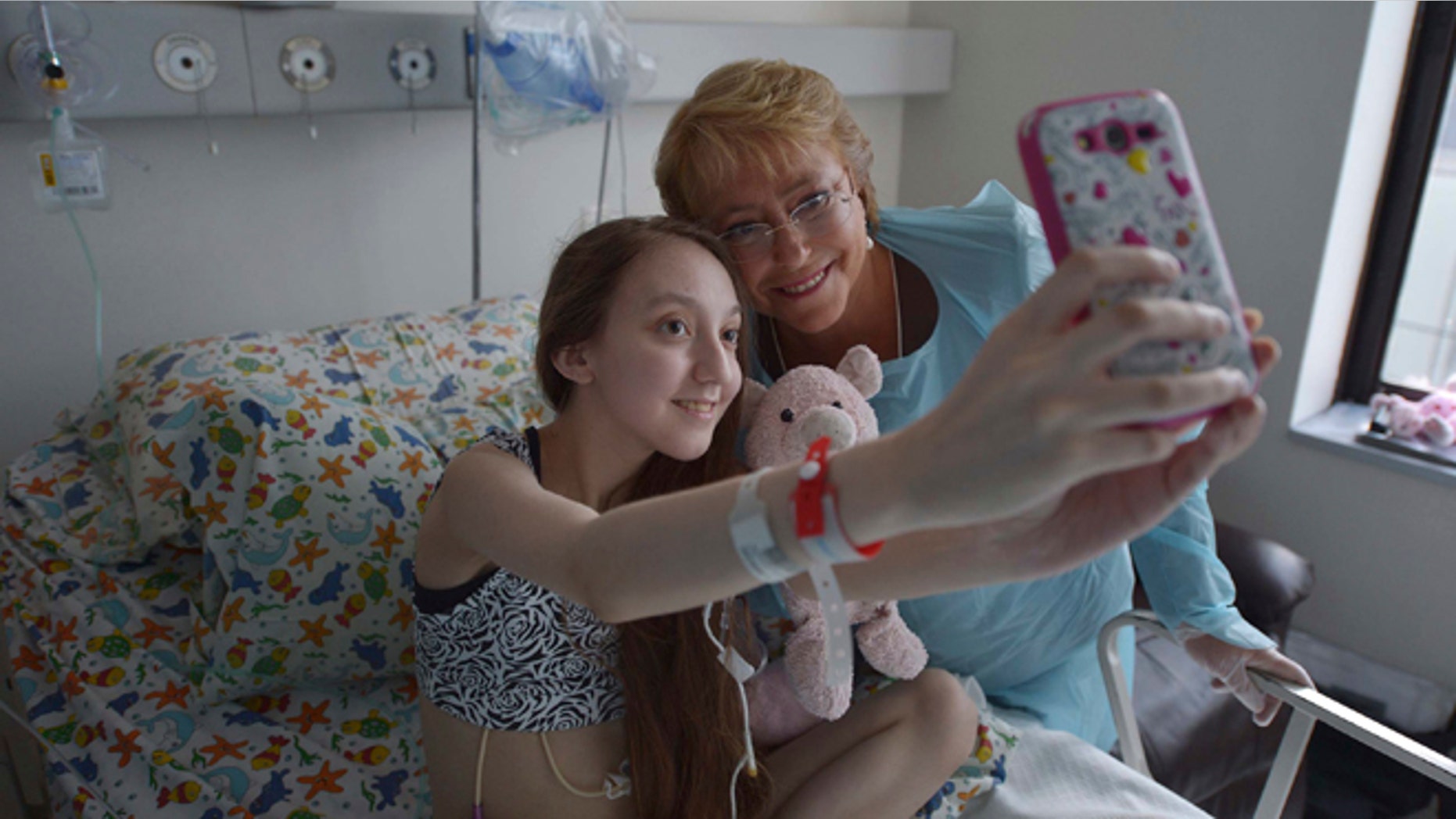 In this Feb 28, 2015 photo released by Chile's Presidential Press Office, Valentina Maureira takes a photo of herself with President Michelle Bachelet, at the Catholic University hospital in Santiago, Chile. The ailing 14-year-old released a video last month in which she asked Bachelet to allow her to be euthanized. Bachelet visited the girl and her family but the government said it could not approve her request. Valentina's father said Sunday, March 22, that people who responded to her plea have led her to change her mind despite her suffering from cystic fibrosis. (AP Photo/Chile Presidential Press Office, Ximena Navarro)