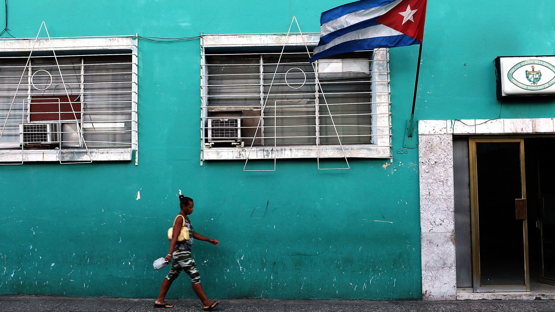 SANTIAGO DE CUBA, CUBA - MARCH 22: A woman walks under a Cuban flag on March 22, 2012 in Santiago de Cuba, Cuba. Fourteen years after Pope John Paul II visited Cuba, Pope Benedict is scheduled to arrive into the communist country on Monday the 26th. Benedict, who will be arriving from Mexico, will conduct a mass in the city of Santiago de Cuba first followed by a mass in Havana before leaving on the 28th. Tensions are high in Cuba between dissidents and the government as activists hope the international exposure of the Papal visit will result in renewed attention to their struggle for greater freedoms. (Photo by Spencer Platt/Getty Images)