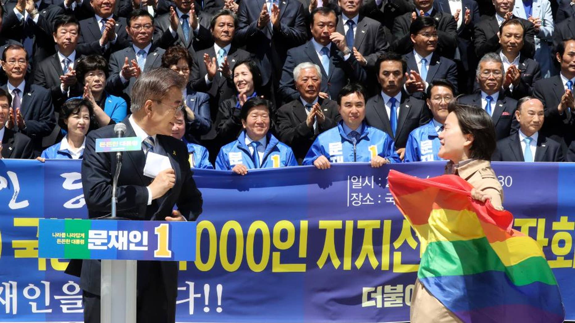 A protester holding a rainbow flag, approaches South Korea's presidential candidate Moon Jae-in from the Democratic Party, left, at National Assembly in Seoul, South Korea, Wednesday, April 26, 2017. South Korean presidential front-runner Moon Jae-in has outraged persecuted sexual minority groups by saying during a television debate that he opposes homosexuality. (Ahn Jung-won/Yonhap via AP)