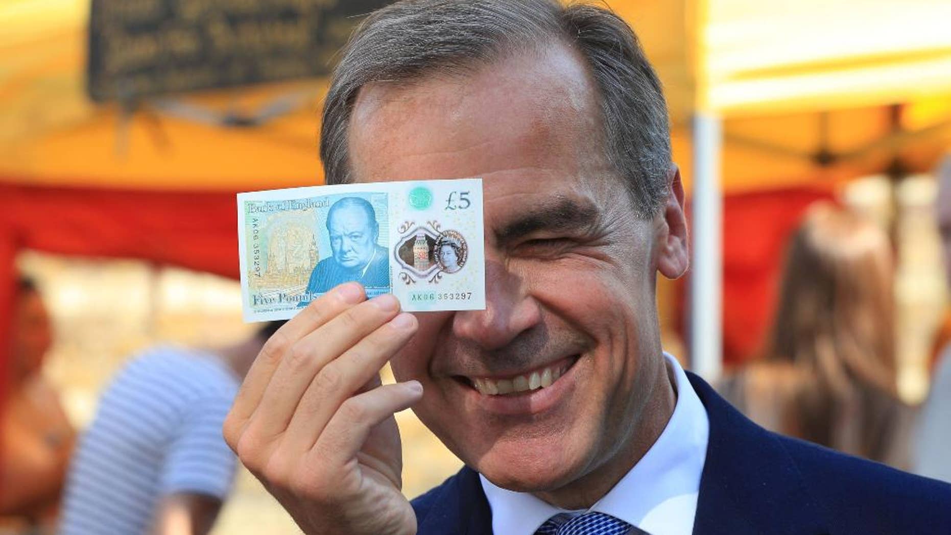 Bank of England Governor Mark Carney holds a new plastic £5 note as he visits Whitecross Street market in London, Tuesday, Sept. 13, 2016. The polymer note is said by the Bank of England to be cleaner, safer and stronger than paper notes, lasting around five years longer. (Jonathan Brady/PA via AP)