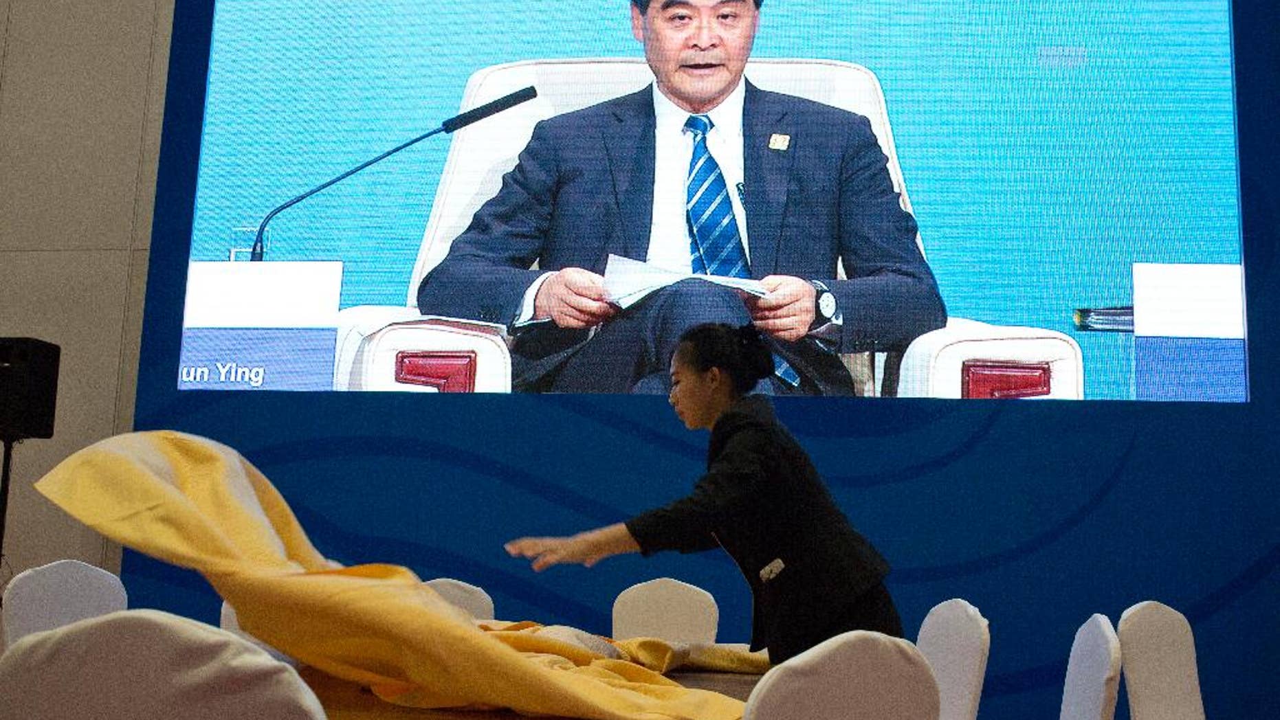 A Chinese waitress lays out a table cloth as Hong Kong's Chief Executive Leung Chun-ying appears on a live broadcast at a dining area of the media center for the Asia-Pacific Economic Cooperation (APEC) Economic meetings held in Beijing, China, Sunday, Nov. 9, 2014. (AP Photo/Ng Han Guan)