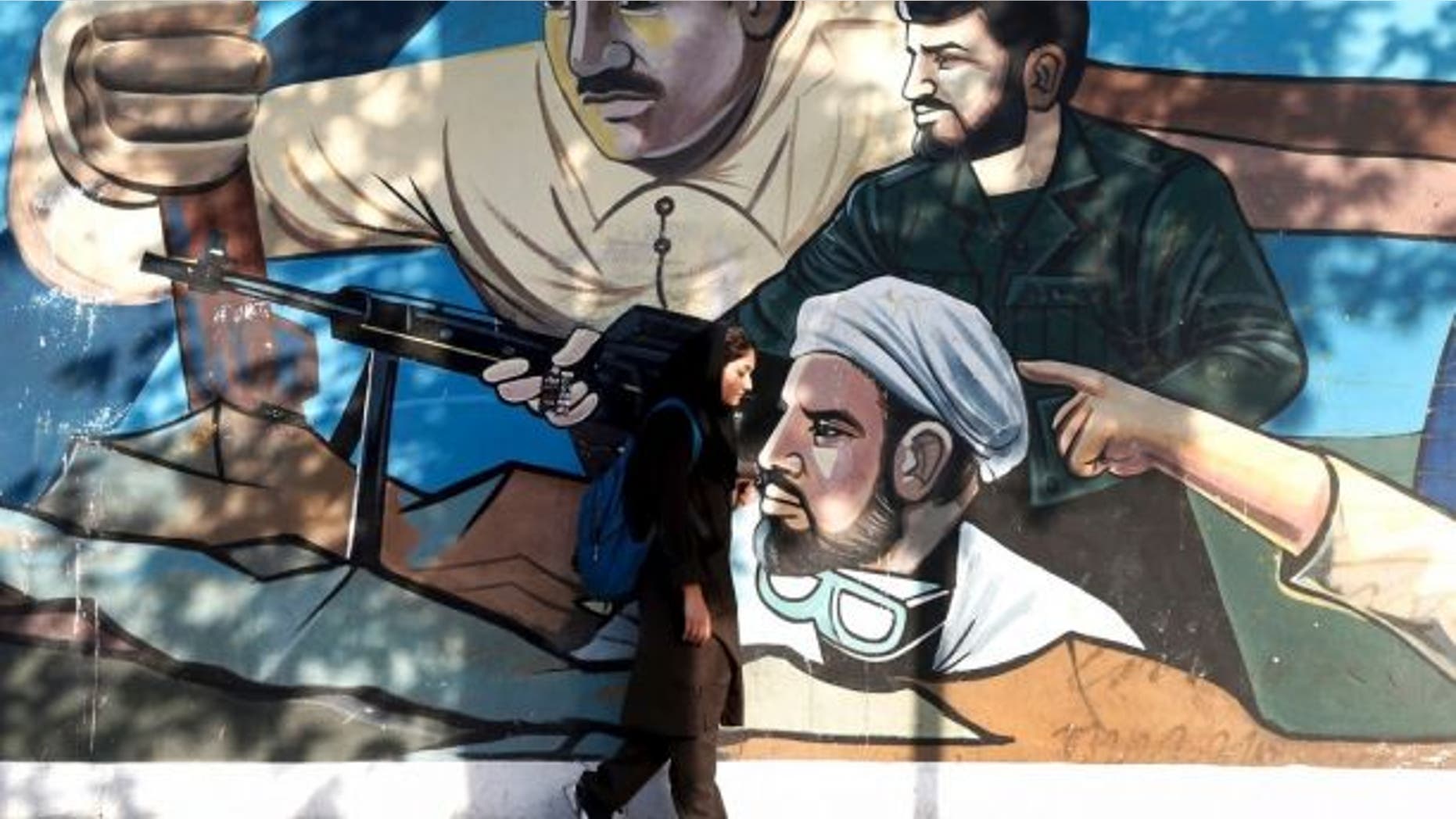 An Iranian woman walks past a mural depicting members of Basij paramilitary force, portraying Iranians' solidarity against their enemies, painted on the wall of a government building at the Felestin (Palestine) Sq. in downtown Tehran