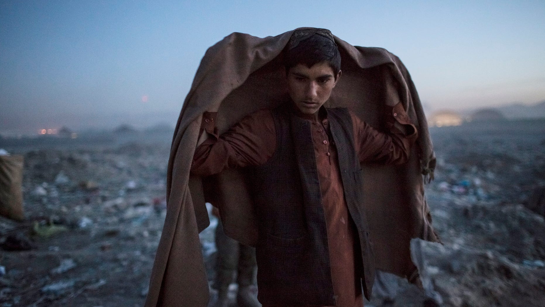 KABUL, AFGHANISTAN - NOVEMBER 14: An Afghan Pashtun boy, who said he was forced from the troubled province of Baglan due to threats from the Taliban, looks on as he winds up for the day after scavenging for recyclables at a garbage dump site on November 14, 2012 in Kabul, Afghanistan. Children working at the garbage site in Kabul said they can make up to 90 Afghans (USD $1.75) per day collecting cans and other recyclable materials for sale. If they were to stay and work in their home province, with limited options for employment, and join the Police or Army, the Taliban threatened they would come for them and their families, they said. (Photo by Daniel Berehulak/Getty Images)