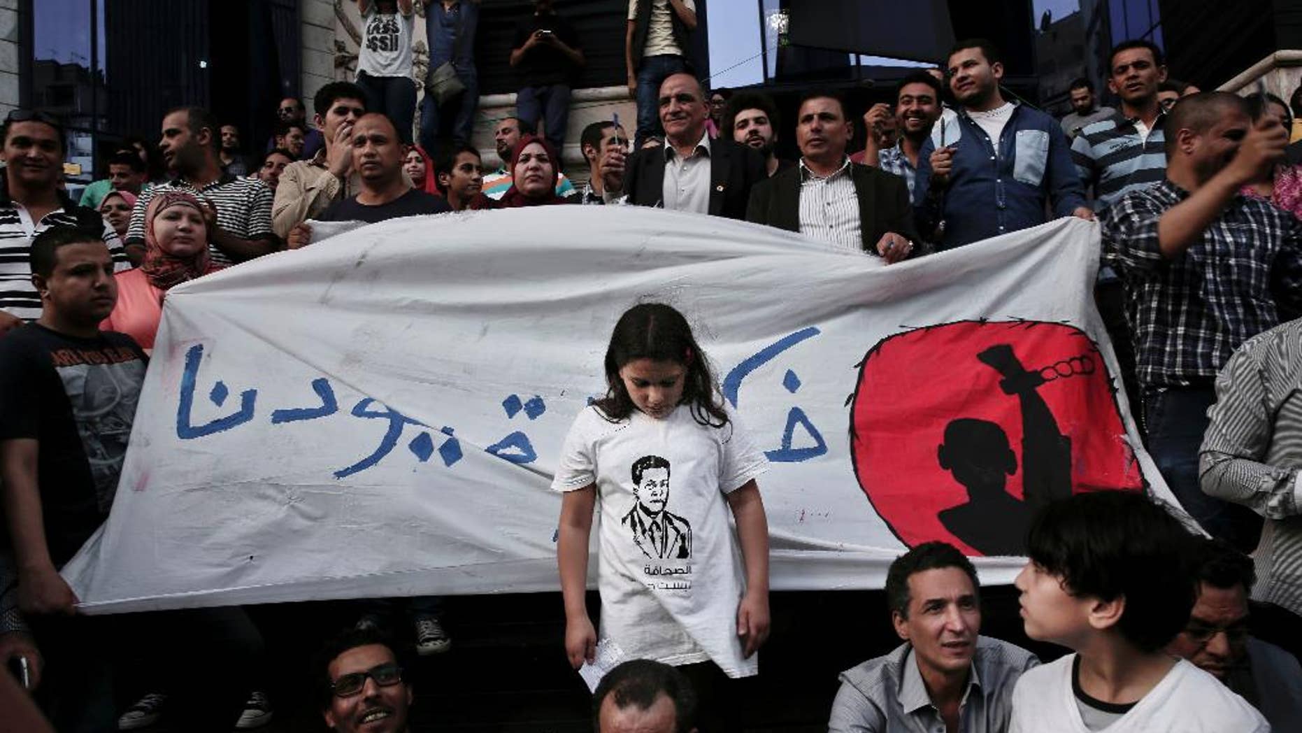FILE - In this Tuesday, May 3, 2016, file photo, a girl stands in front of a banner with Arabic that reads, "remove our shackles," during a protest to mark World Press Freedom Day in front of the Press Syndicate in Cairo. The lawyer for three Egyptian journalists who were arrested while conducting street interviews said on Sunday that they were beaten and tazered by security officers during questioning at a central Cairo station. Fatma Serag told The Associated Press the three _ Hamdy Mokhtar, 38, Mohammed Hassan 18, and Osama el-Bishbishi, 35 _ were accused of supplying Turkey-based television networks linked to the now-banned Muslim Brotherhood group with “negative” videos of life under the rule of President Abdel-Fattah el-Sissi. (AP Photo/Nariman El-Mofty)