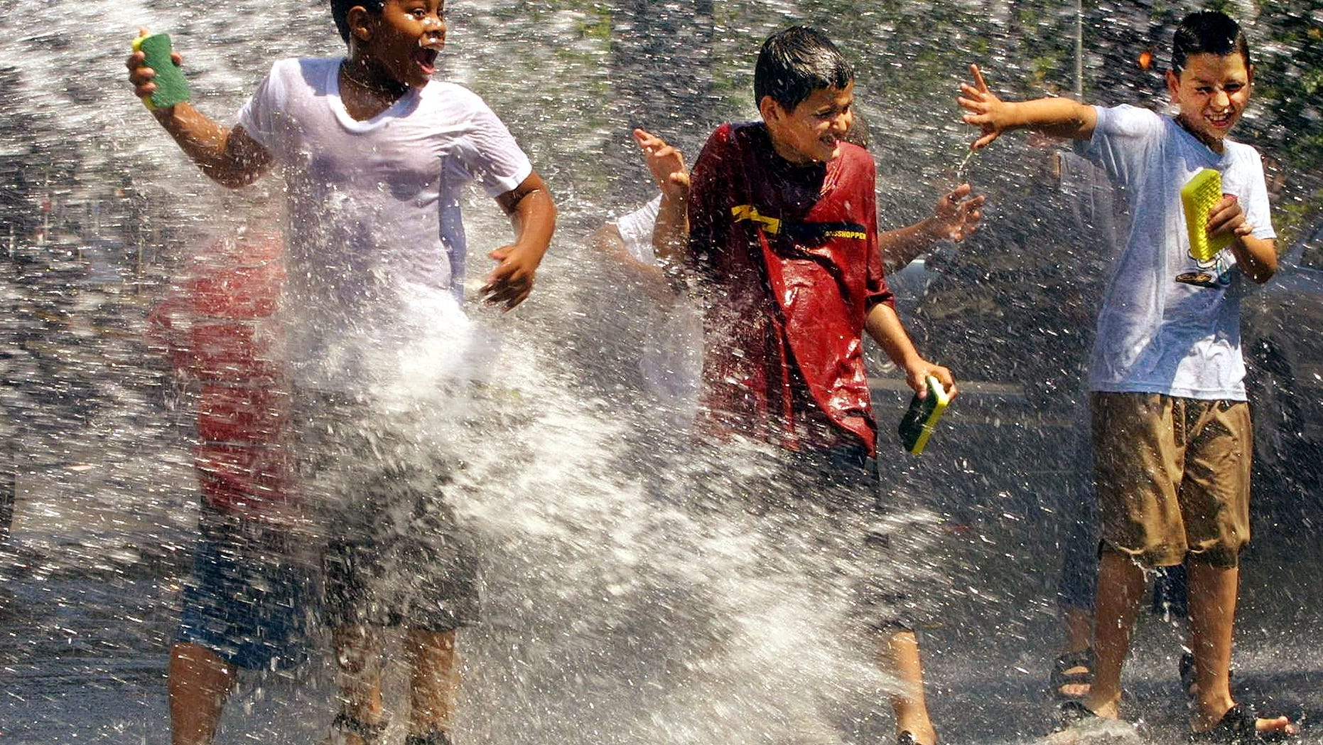 Children use a fire hydrant to cool off while washing cars in Washington Heights, New York City.