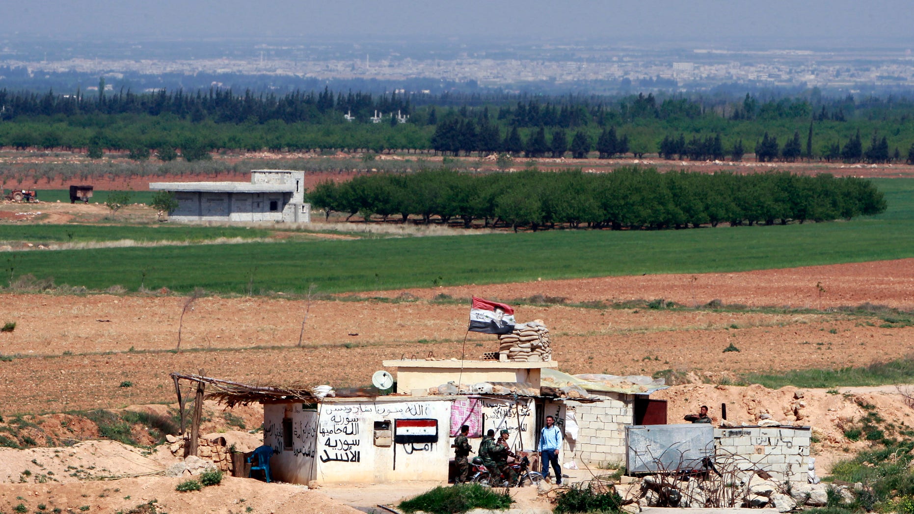 Syrian soldiers at a Syrian army post as seen from the Lebanese border village of al-Qasr, Lebanon, Friday, April 12, 2013. Syrian warplanes and troops battled rebels near the border with Lebanon as part of a widening government counteroffensive to recapture territory along strategic border areas and near the capital Damascus. Written on the army post are the words “only God, Syria and Bashar” and “God is protecting Syria.” (AP Photo/Bilal Hussein)