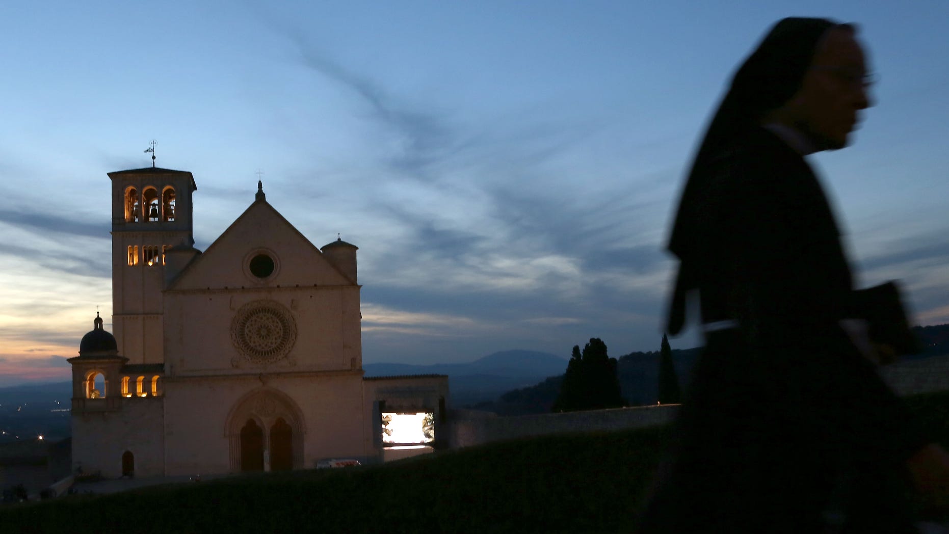 ASSISI, ITALY - OCTOBER 03: A nun walks past the Sacro Convento and Saint Francis Basilica prior to Pope Francis' visit on October 3, 2013 in Assisi, Italy. The residents of Assisi have been busy all week preparing for the arrival of Pope Francis, the first Bishop of Rome to take the name of Assisi's most famous son. Pope Francis is due to venerate the tomb of San Francesco of Assisi at the crypt of the Upper Basilica of Saint Francis tomorrow during his one-day visit to the city. (Photo by Franco Origlia/Getty Images)