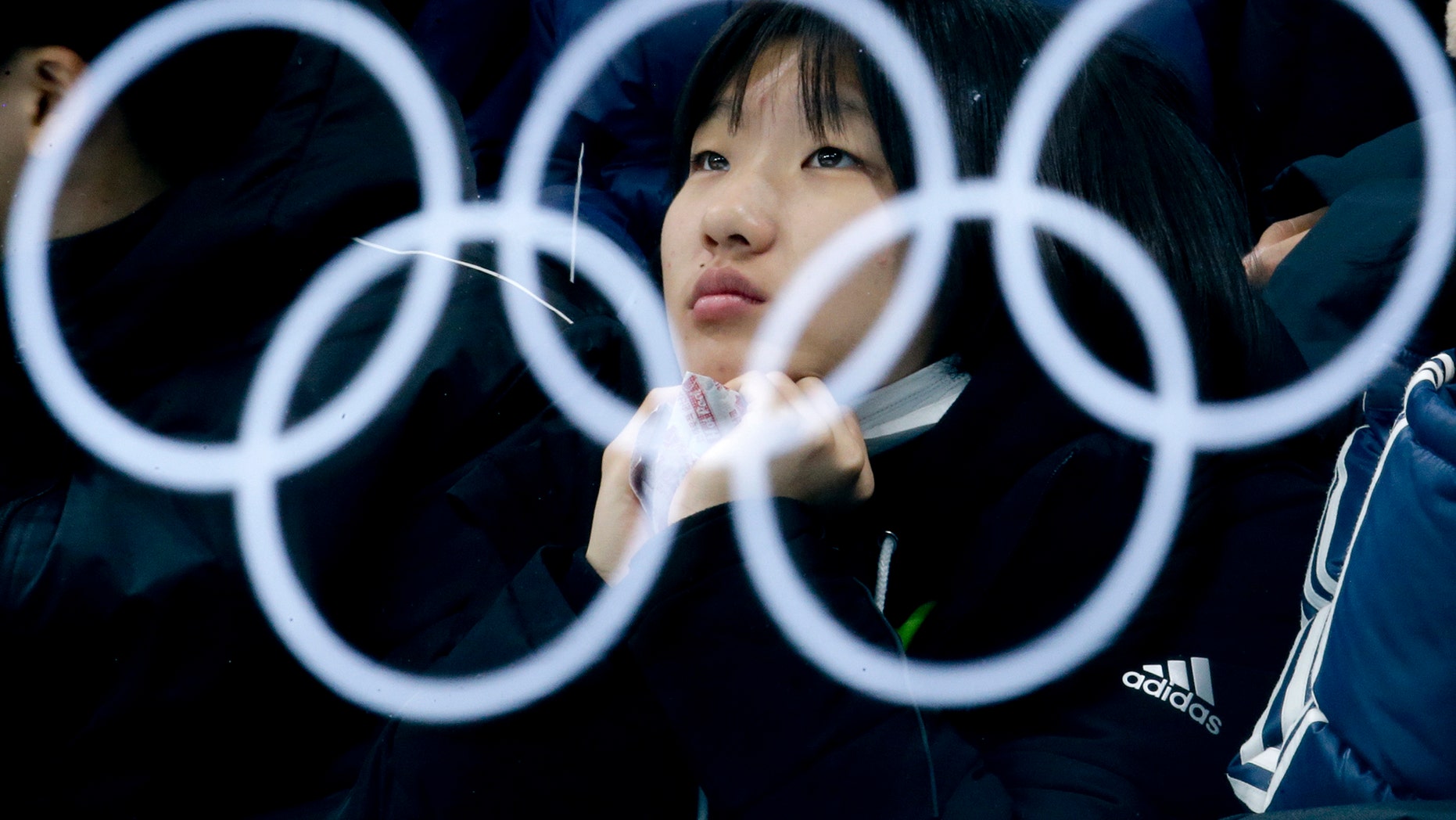 The Olympic rings are reflected in a glass as a spectator watches the mixed doubles semi-final curling match between Canada and Norway at the 2018 Winter Olympics in Gangneung, South Korea, Monday, Feb. 12, 2018. (AP Photo/Natacha Pisarenko)