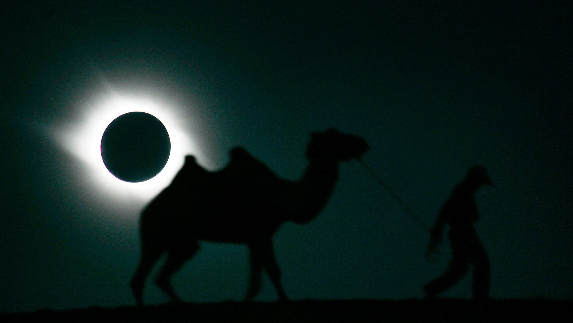 A man and his camel walk past as the sun is blocked by the moon during a solar eclipse in Gaotai, Gansu province August 1, 2008. REUTERS/Aly Song (CHINA) - RTR20JDU